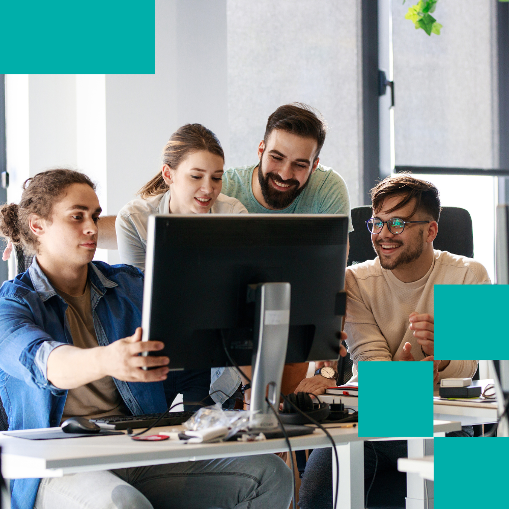 Four young professionals smiling and collaborating around computer in office setting