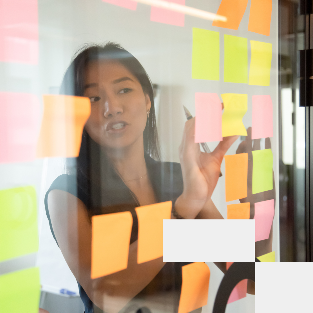 Woman writing on glass wall with colorful sticky notes in collaborative office environment