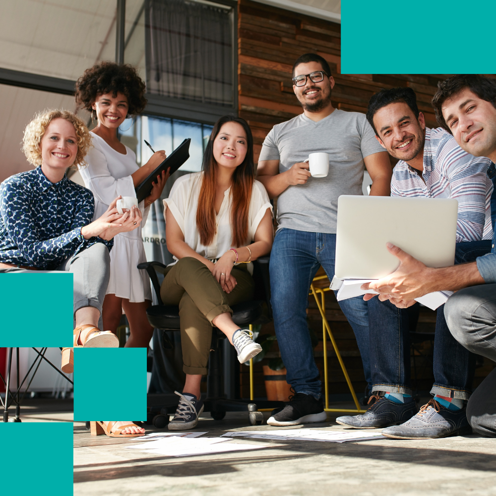 Group of six diverse young professionals in office smiling, holding coffee mugs, laptop, and notepad
