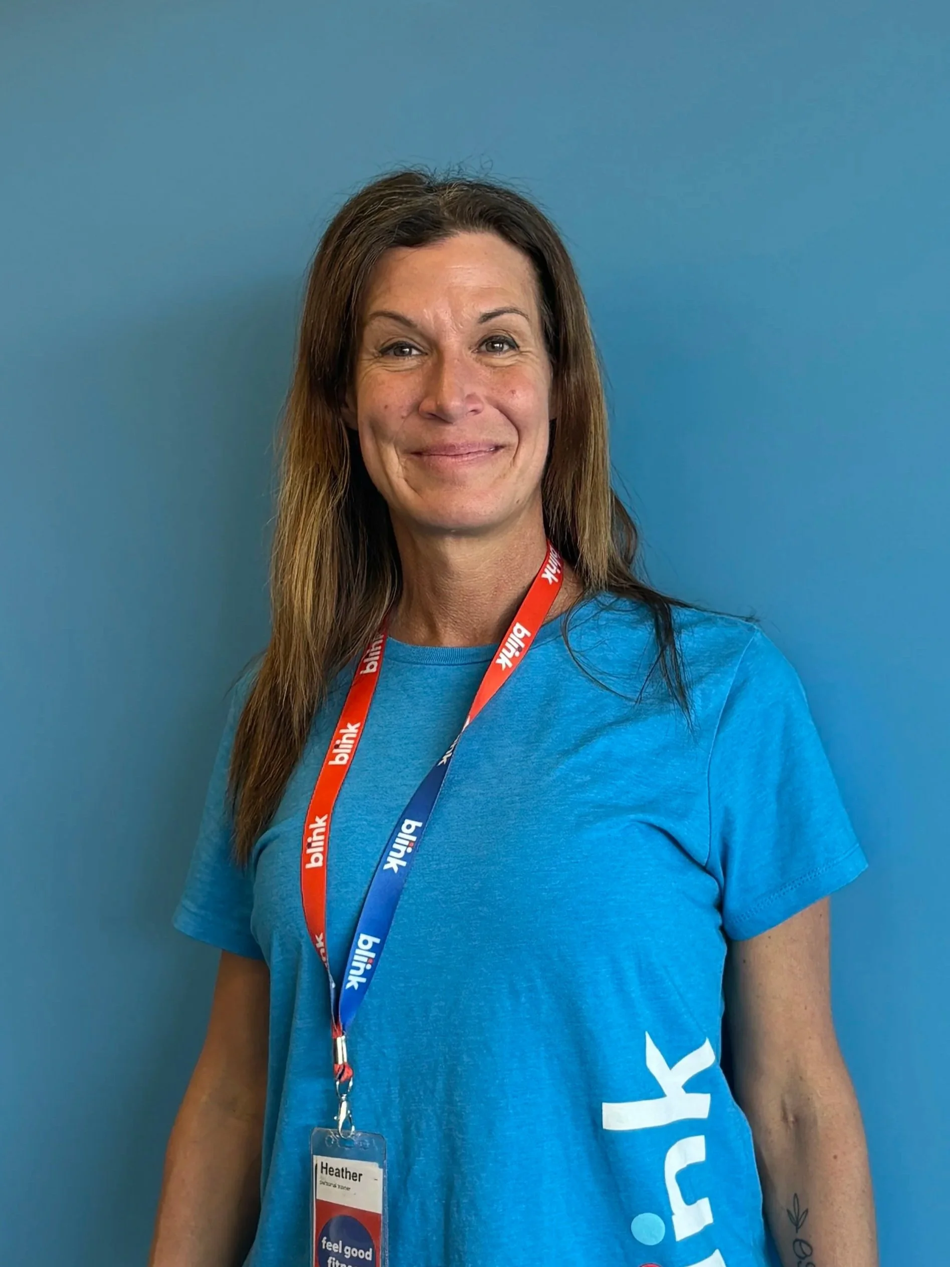 Woman in blue t-shirt and beanie smiling in front of a blue wall.