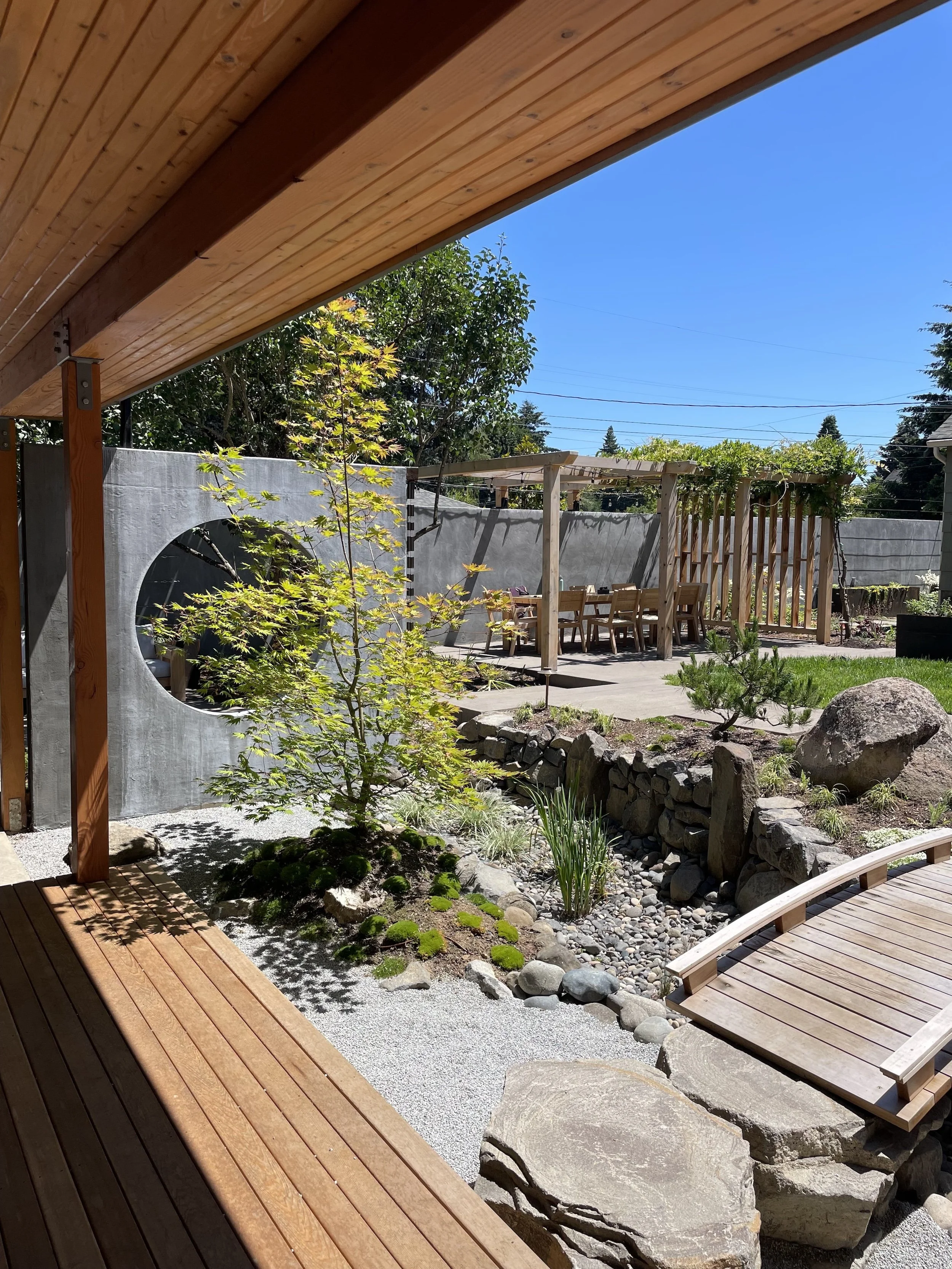 Wooden deck overlooking a landscaped backyard with trees, rocks, and outdoor dining area