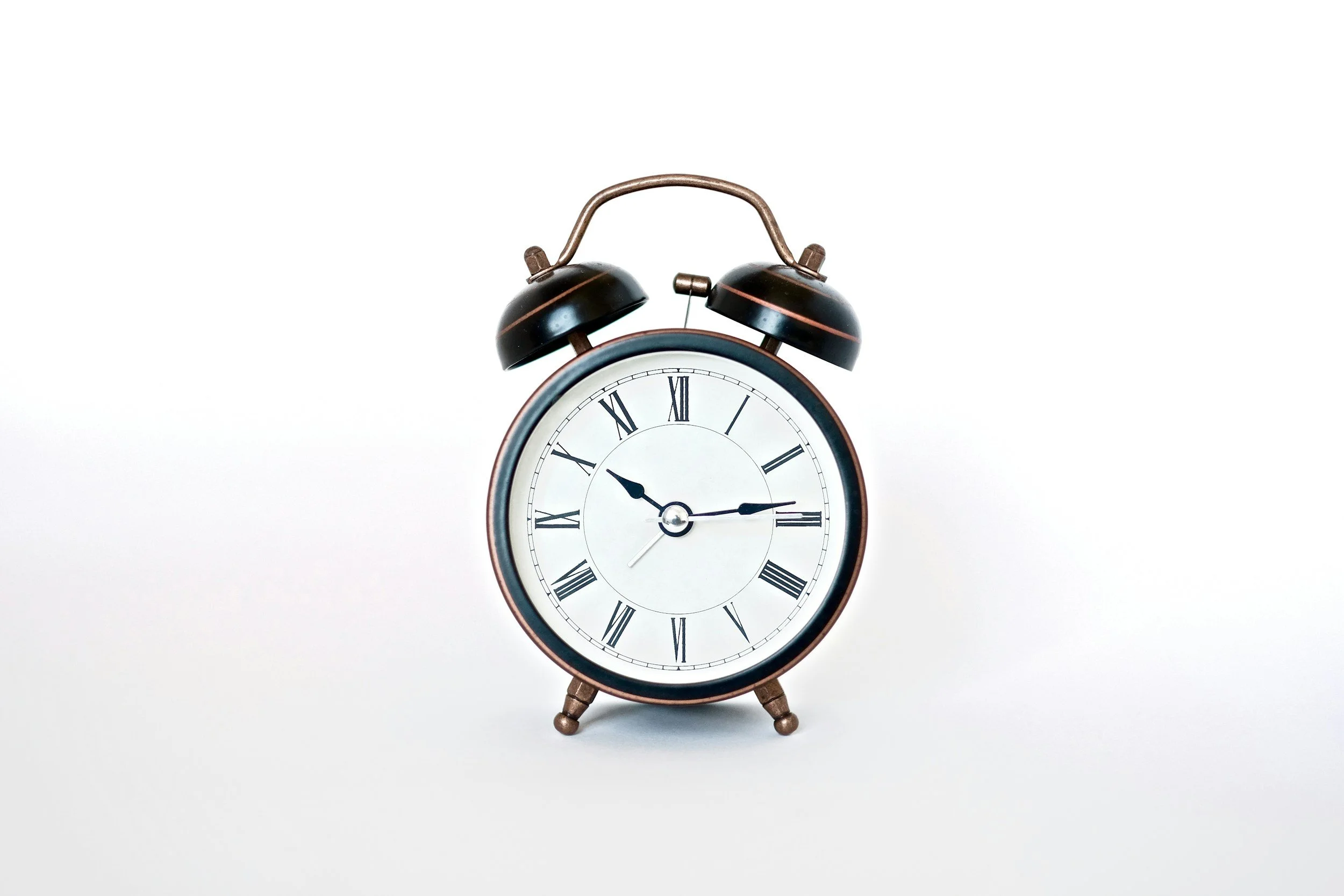 A vintage alarm clock with twin bells on top and Roman numerals on the face, showing the time as 10:14, against a plain white background.