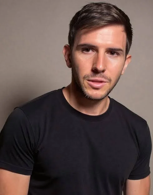 A young man with brown hair wearing a black t-shirt, looking at the camera against a plain gray background.