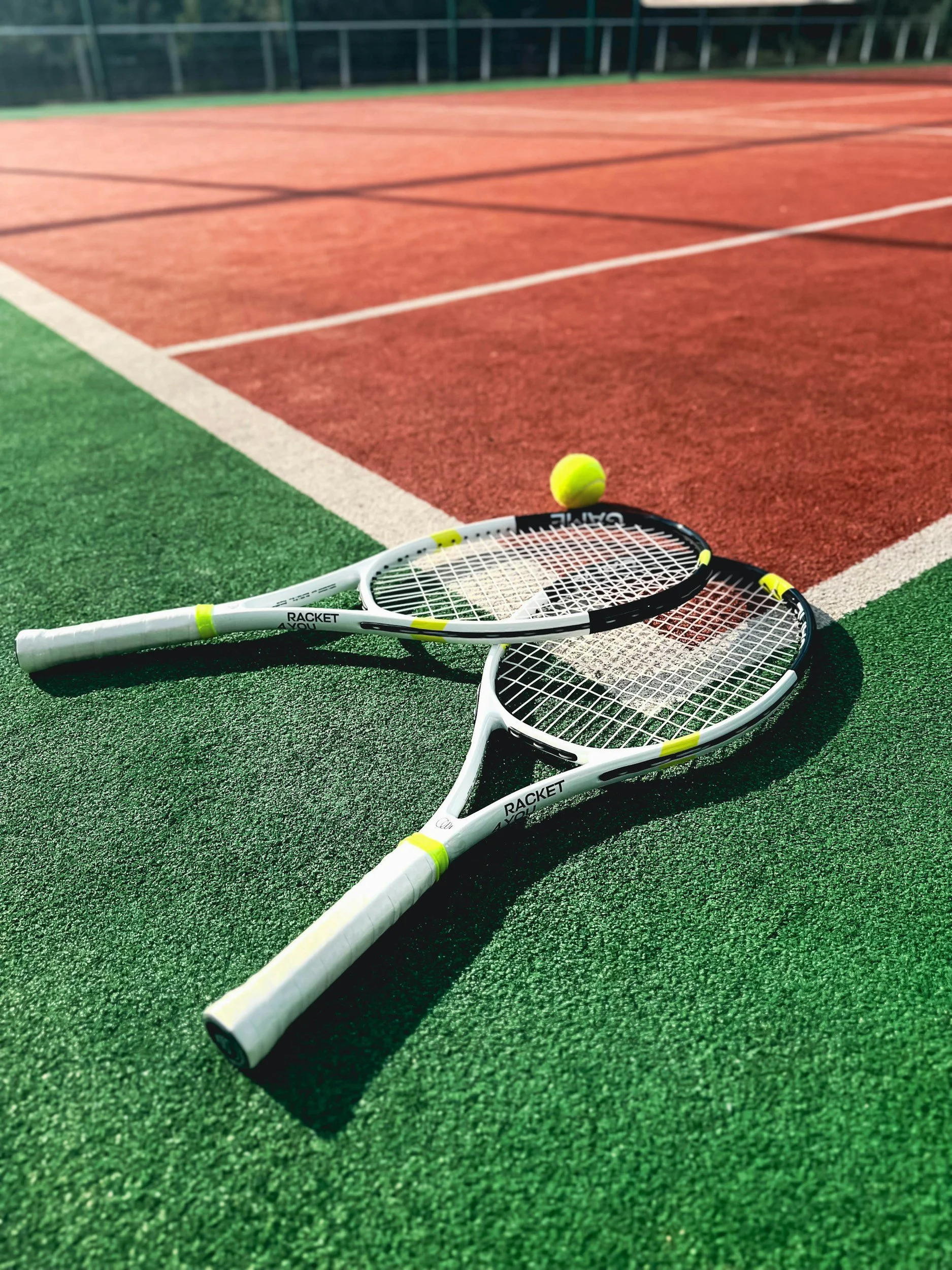 Two tennis rackets and a tennis ball on a green and red tennis court.