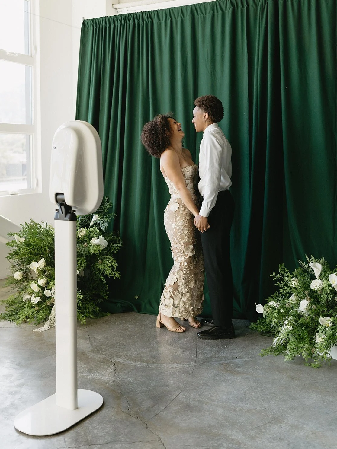 A couple stands joyfully together in front of CLT Photo Booth Magik’s green back drop setup at a birthday party in Gastonia.