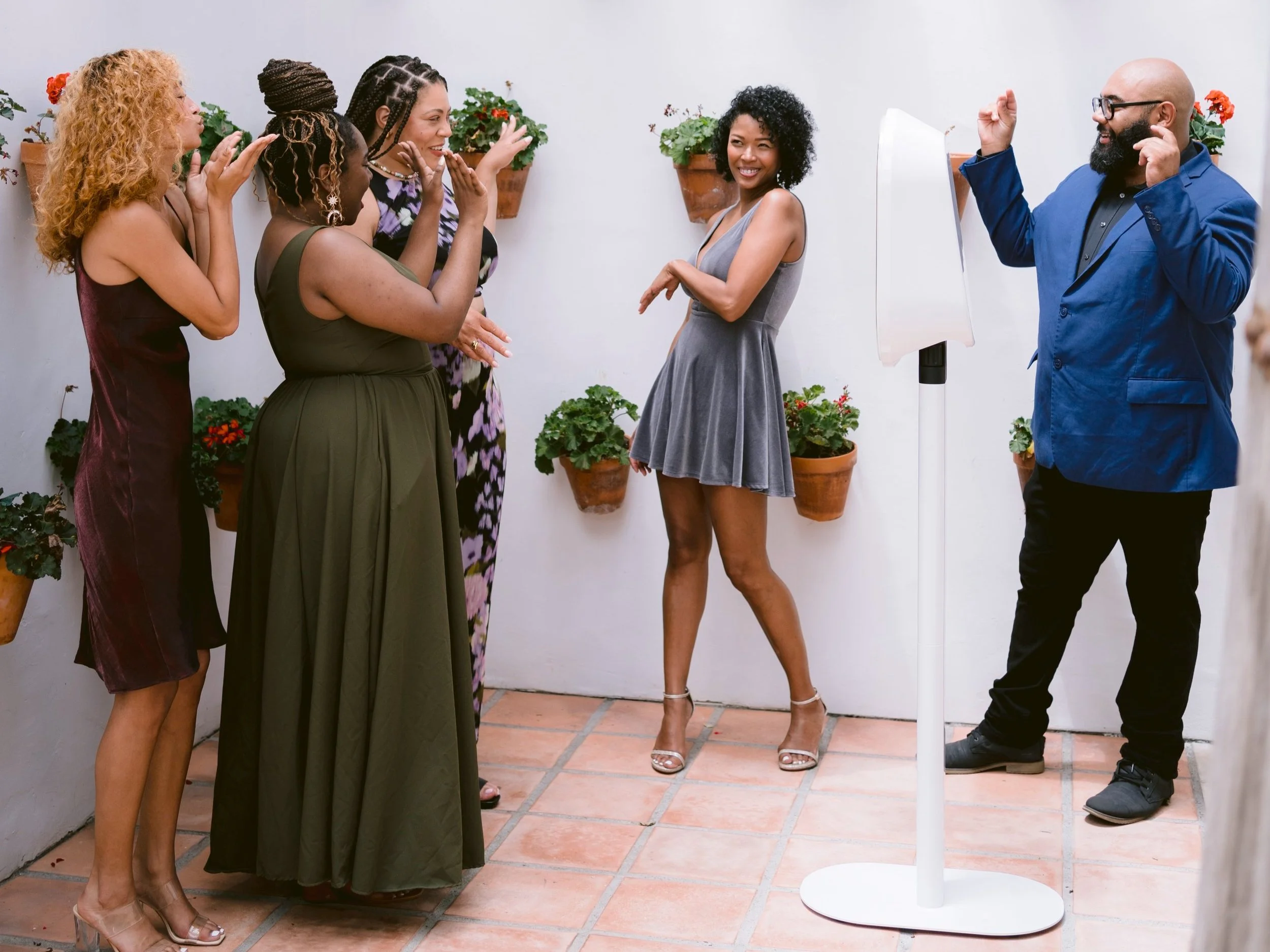 Group of people posing around CLTPhotoBoothMagik’s photo booth at a party, with decorative plants on the wall.