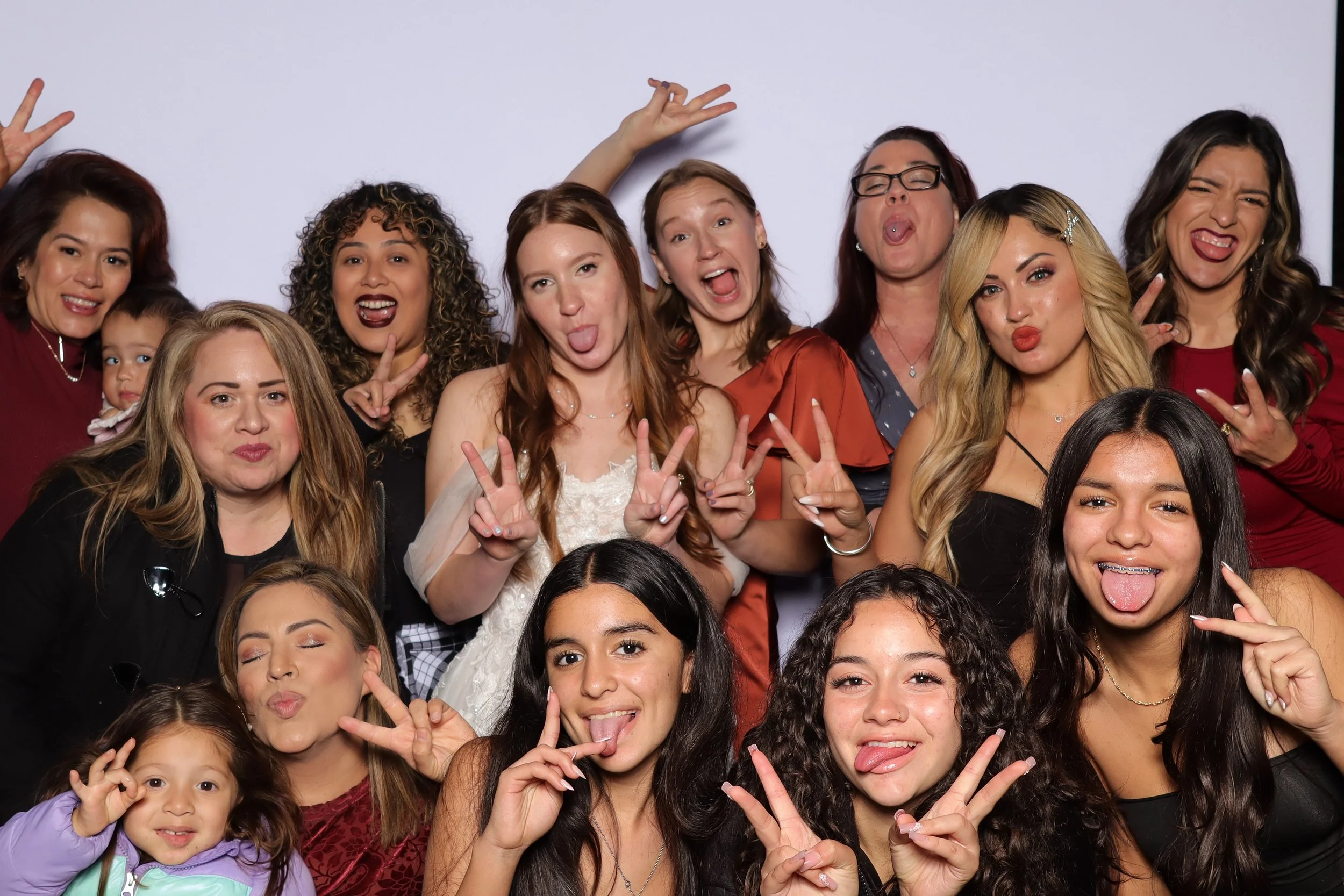 Group of women and children making funny faces and peace signs in front of a plain white background.