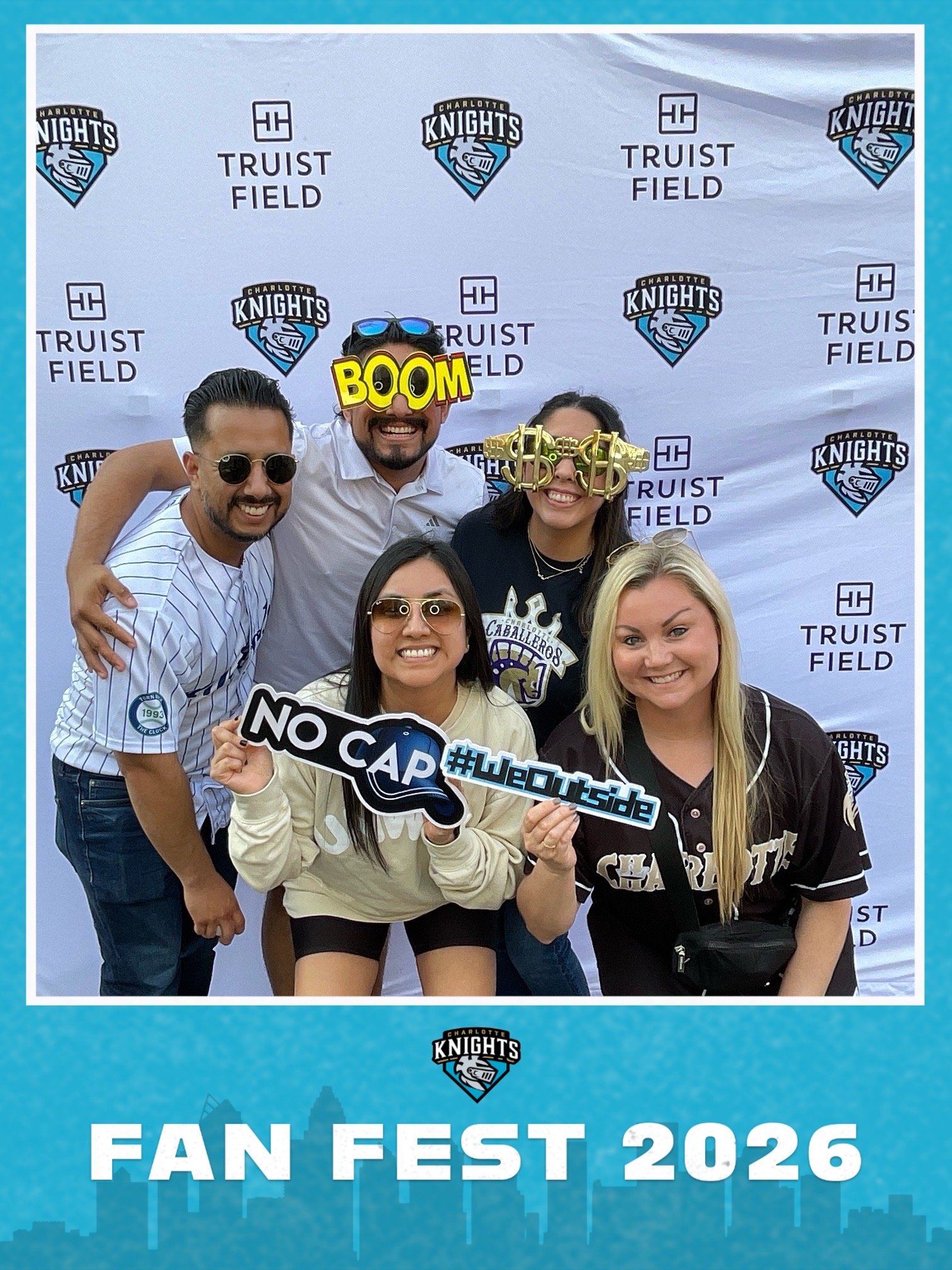 A group of five people at Charlotte Knights Fan Fest 2026, posing for a photo in front of a banner with the team logo and event name. They are smiling, with some wearing novelty glasses and holding signs.