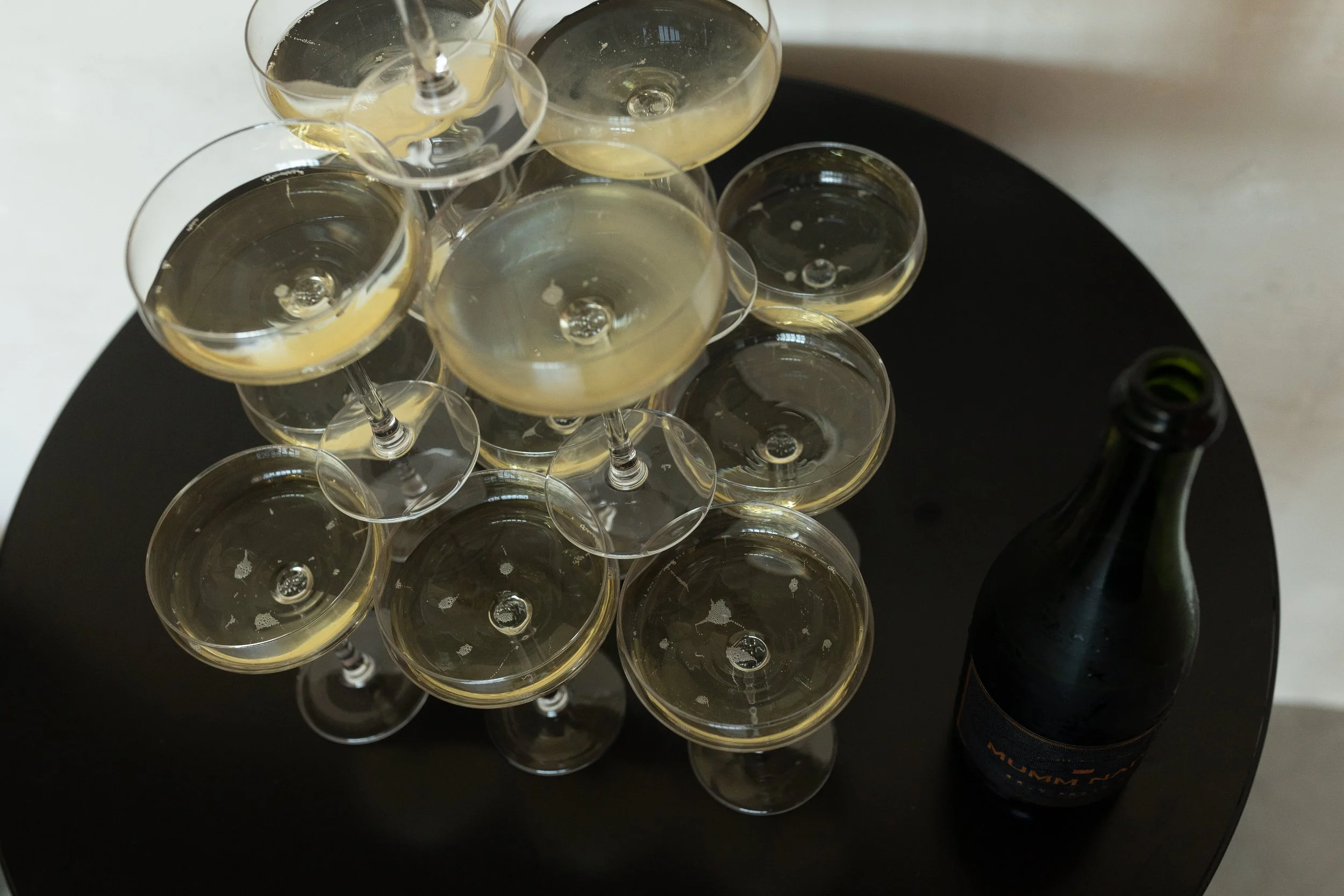 Champagne tower of filled glasses and an empty champagne bottle on a black table.