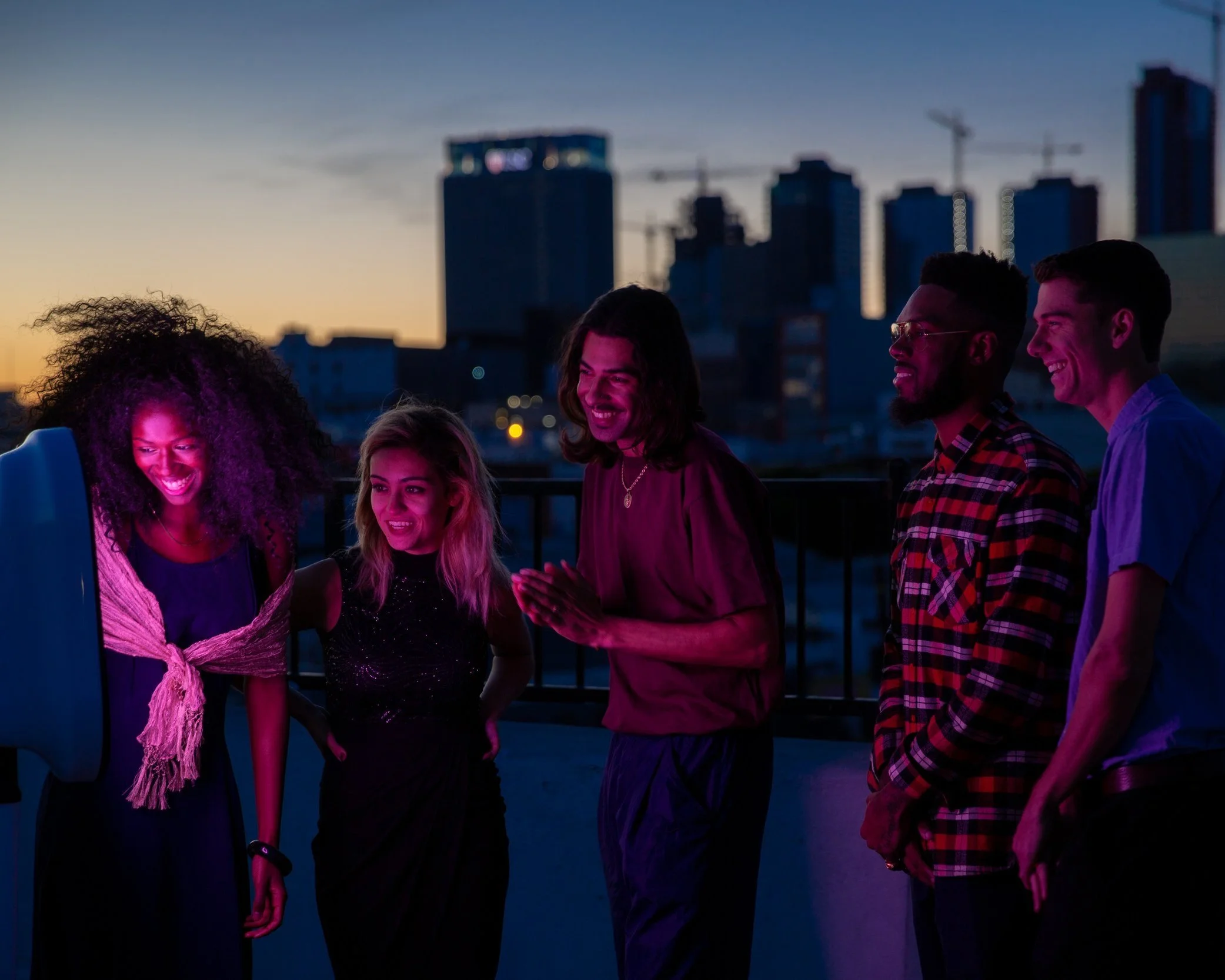 Group of friends smiling and socializing at Aura Rooftop Charlotte , NC with colorful Charlotte city skyline in the background.
