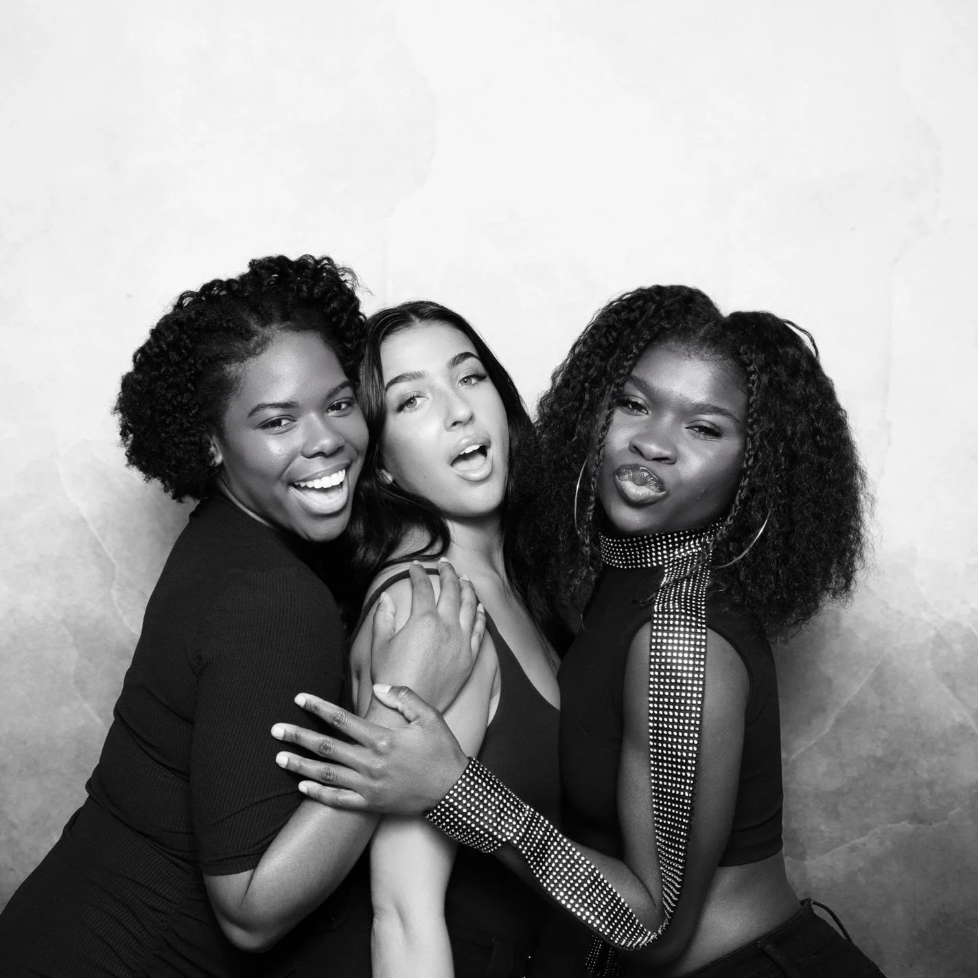 Three women in black-and-white photo, smiling and posing with a joyful expression.