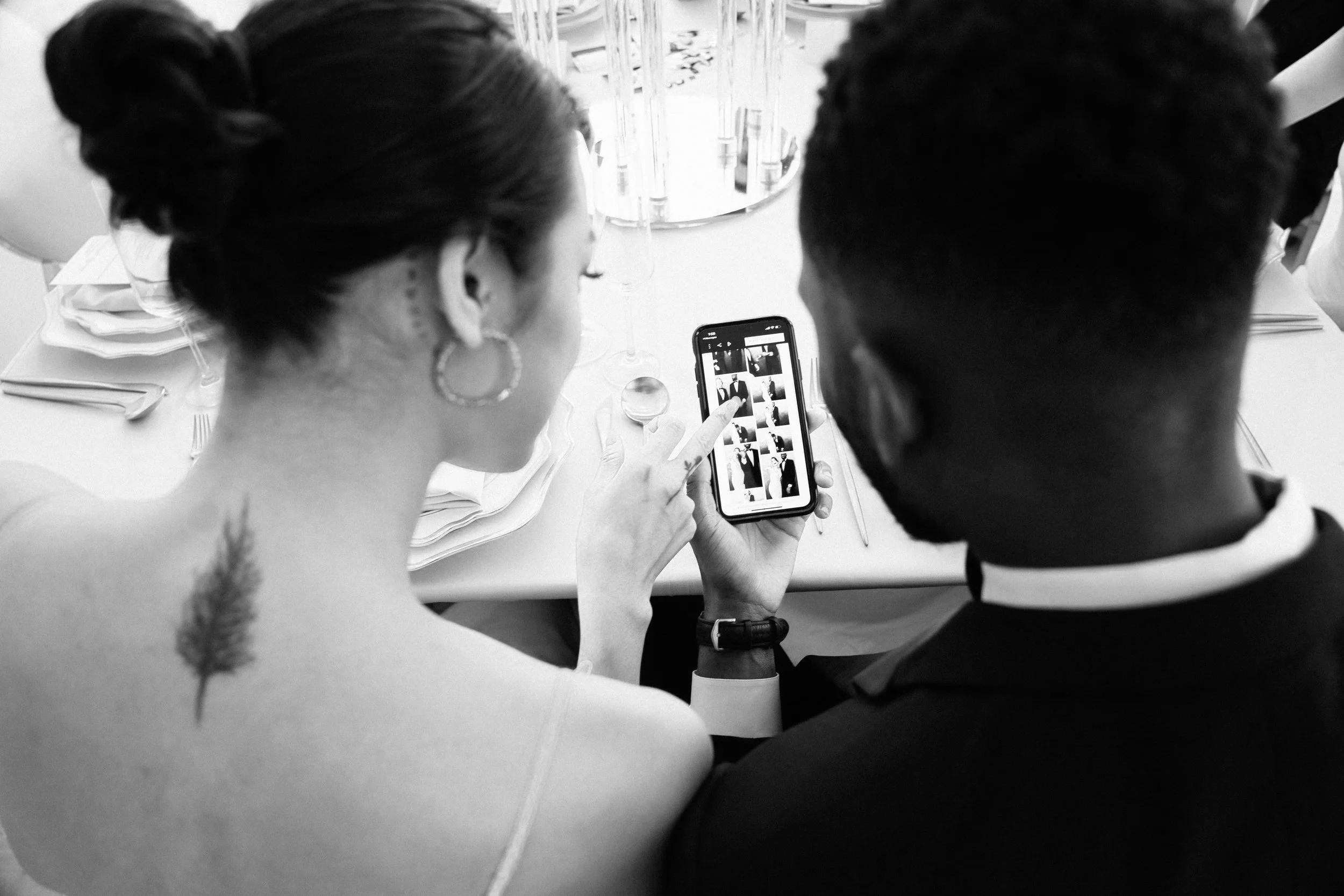 A bride and groom looking at the photo booth live gallery from their wedding on their smartphone.