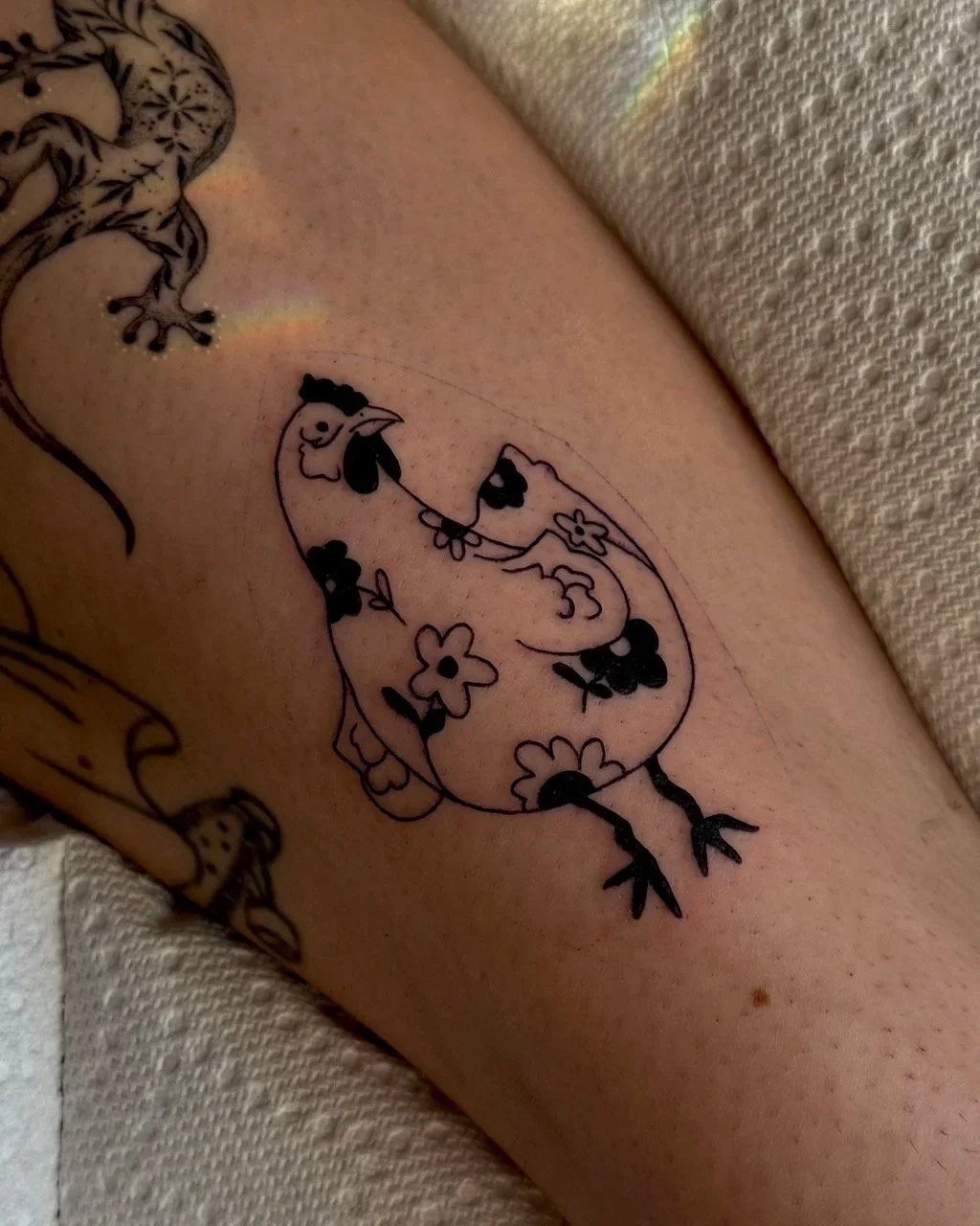 Tatouage d'une poule stylisée avec un motif de fleurs sur la jambe d'une personne.
