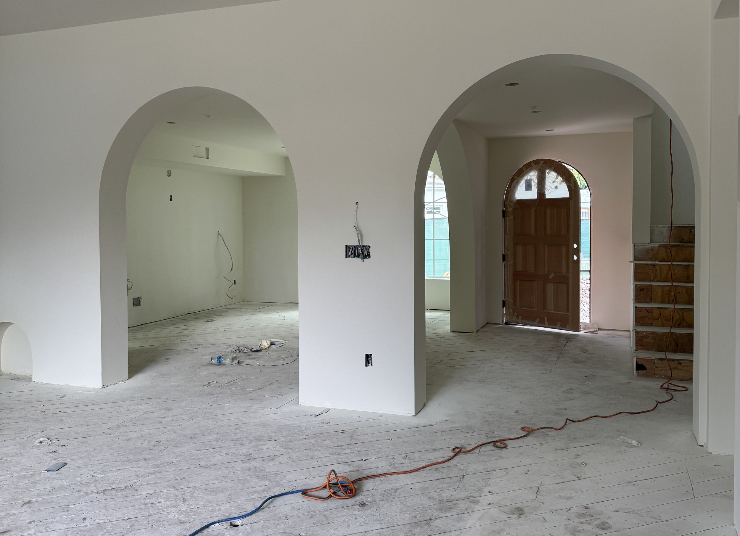 Interior view of a house under construction with unfinished walls, framing, and electrical wiring visible.
