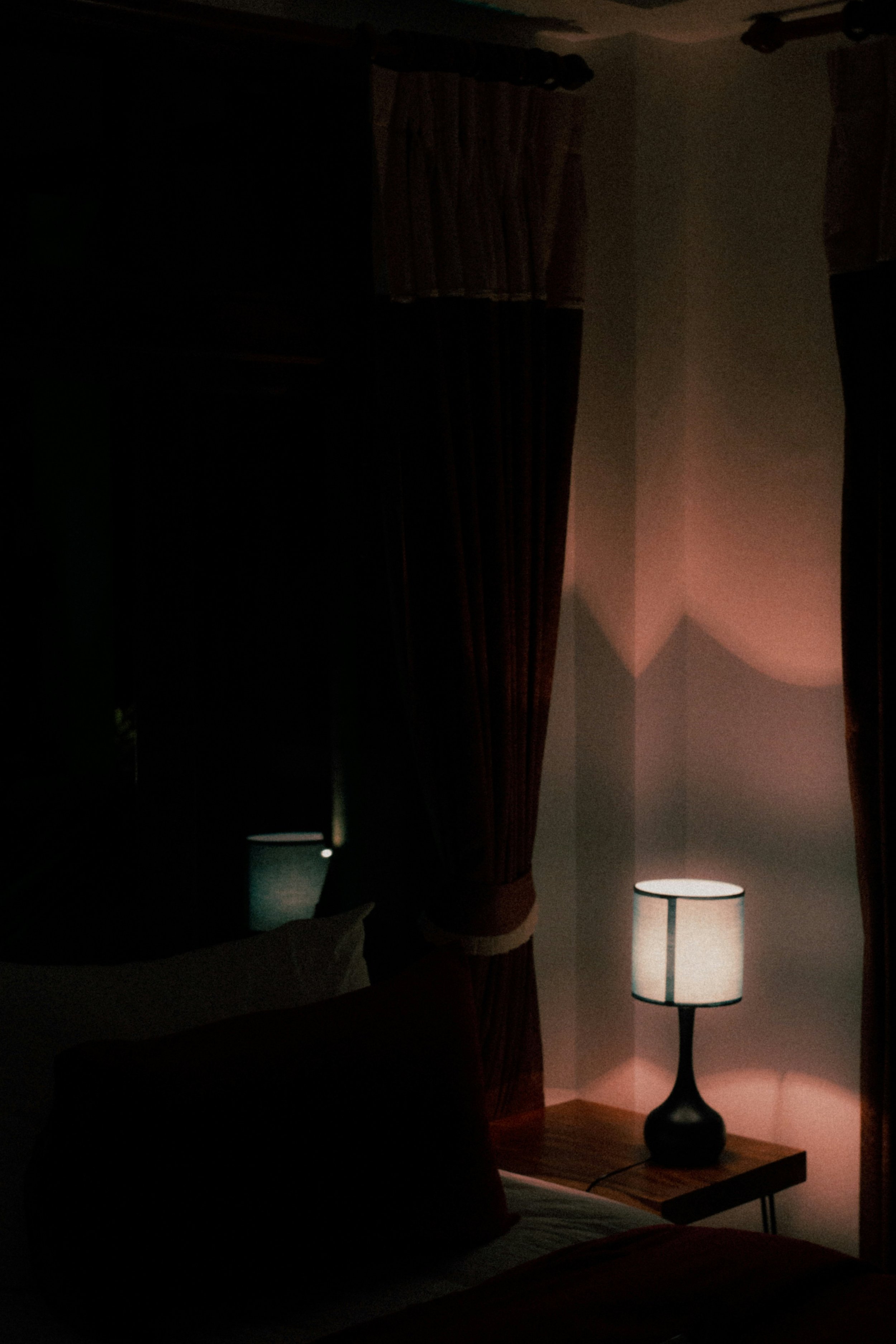 Ein dunkles Schlafzimmer mit einem Bett, einem Nachttisch und einem Lampenschirm, der ein warmes Licht abgibt.