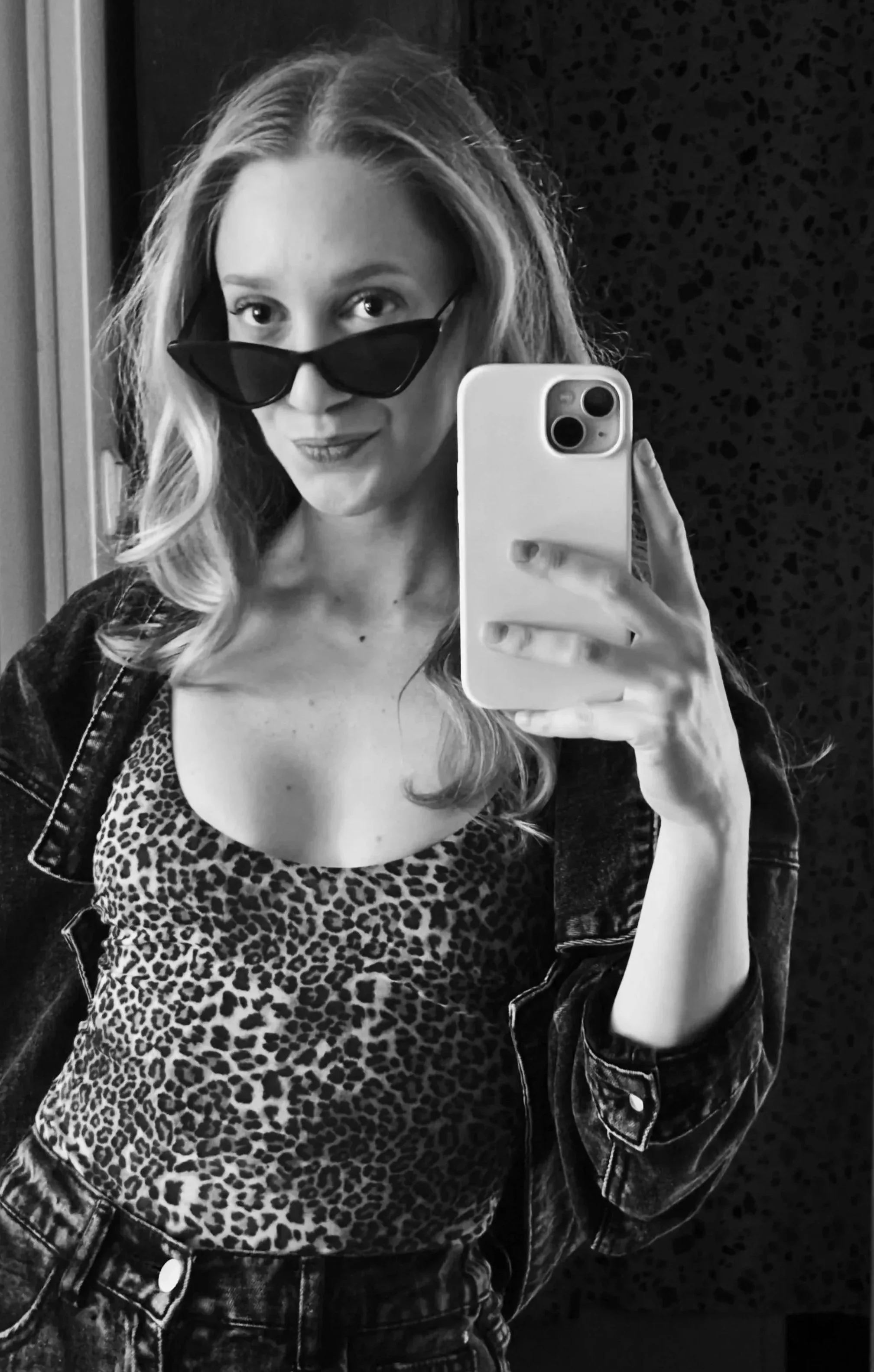 Frau macht Selfie mit schwarz-weiß Foto in Spiegel, trägt dunkle Sonnenbrille, Leopardenmuster-Top und Jacke.