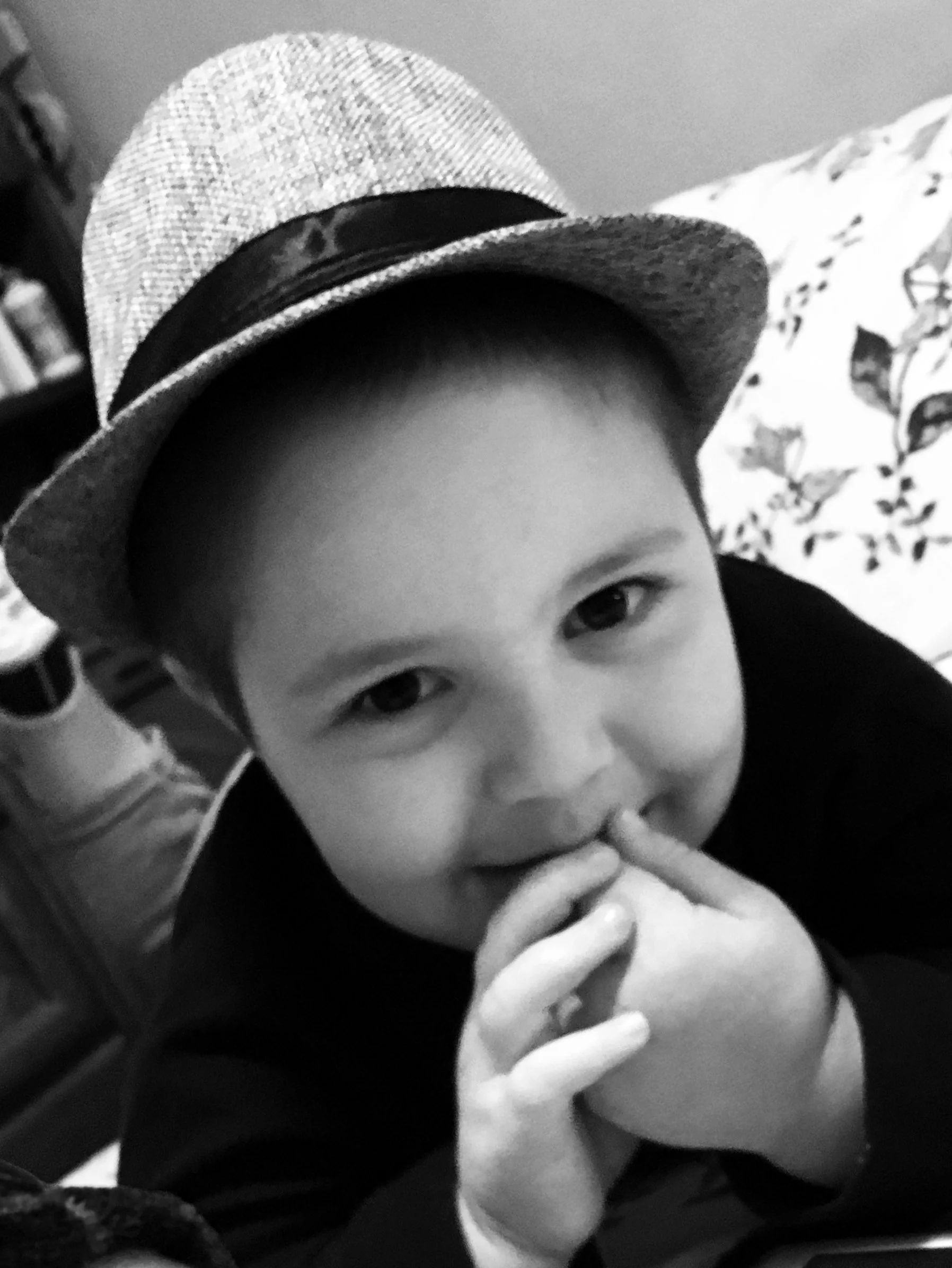 small boy wearing a fedora hat smiling at the camera with his hands held to his mouth
