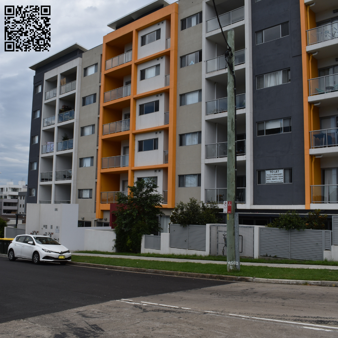 Multistory apartment building with gray, white, and orange exterior walls and balconies, under an overcast sky.