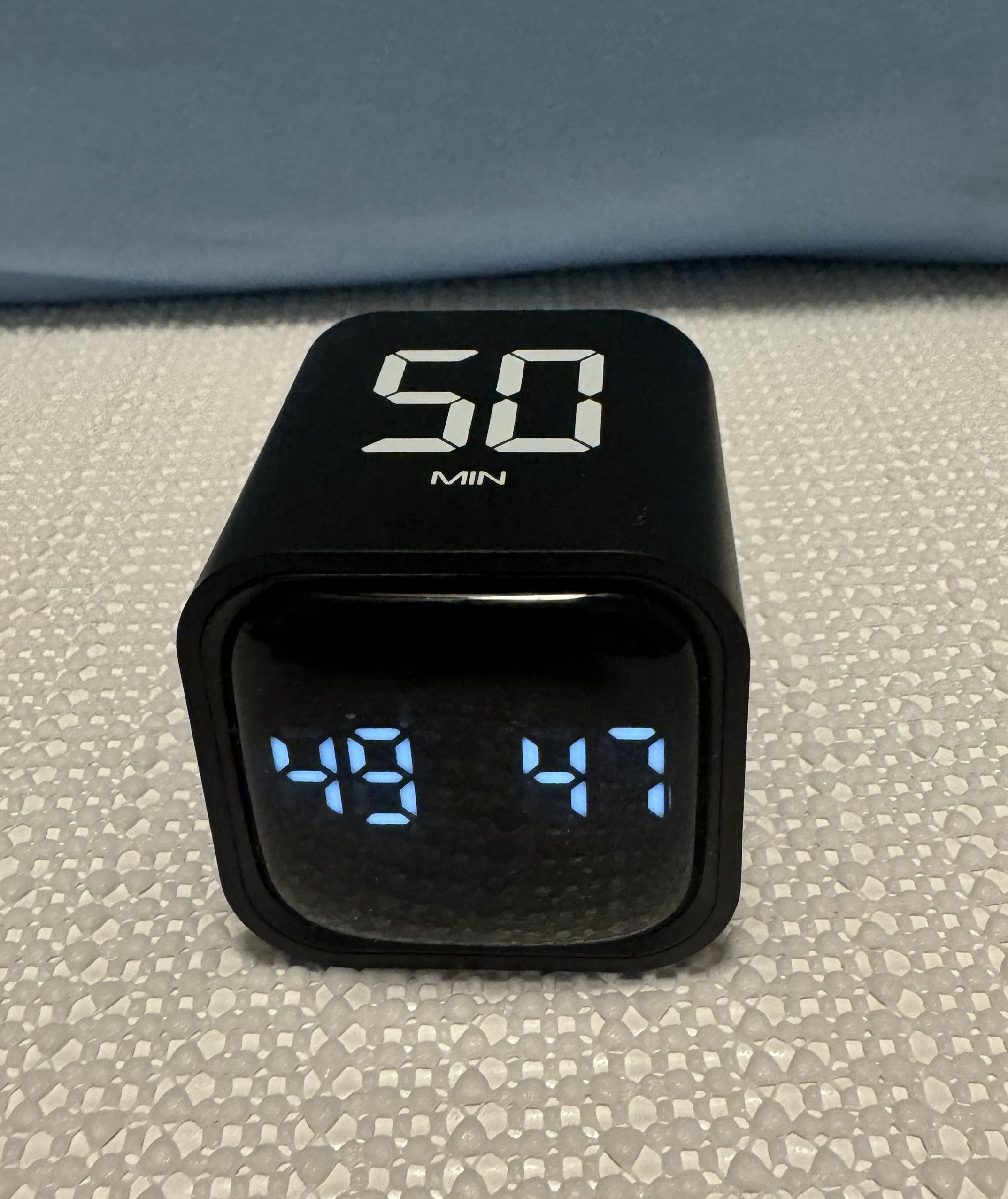 Digital clock showing 49:47 and a timer set for 50 minutes, placed on a speckled surface.