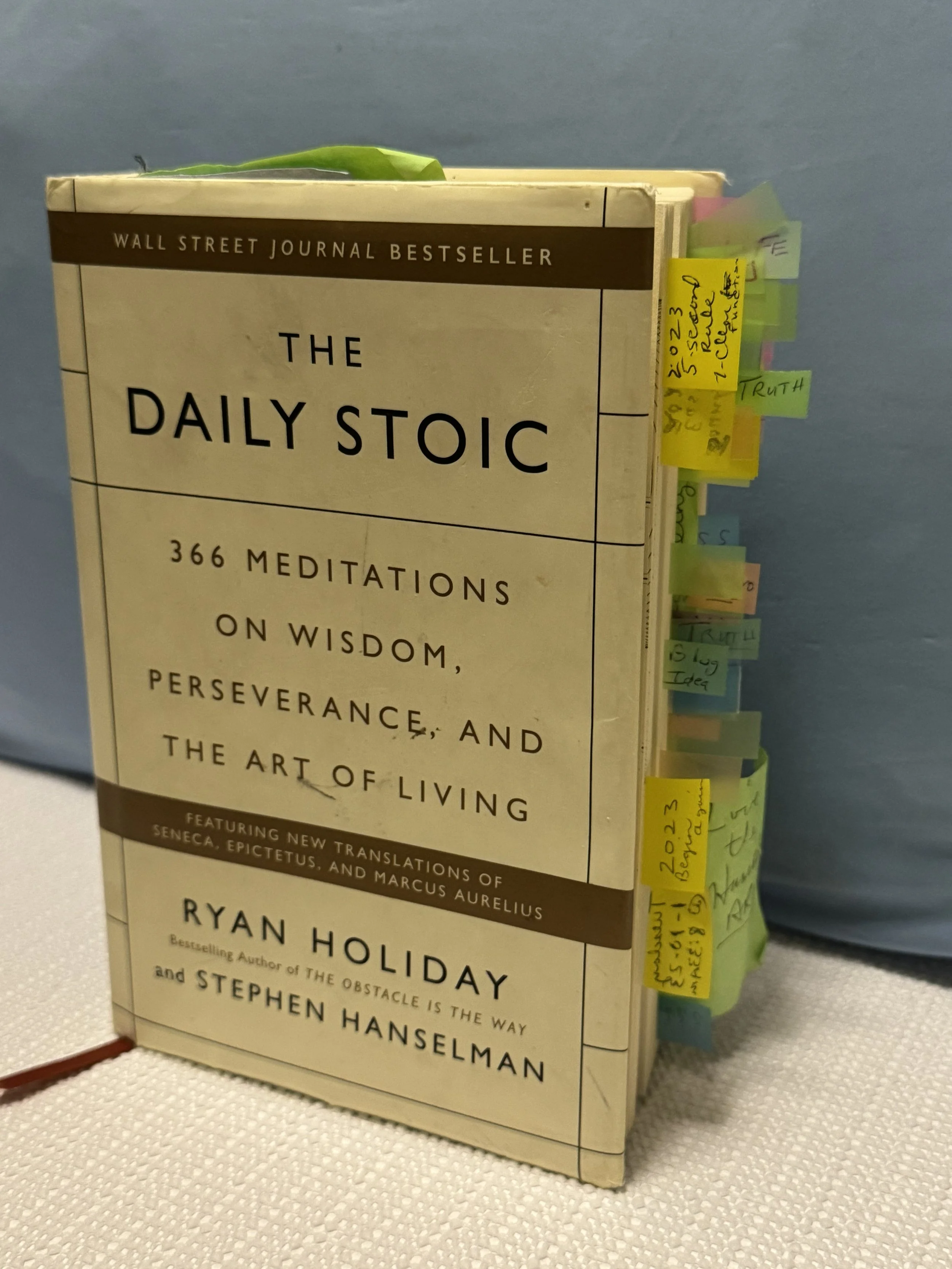 A book titled 'The Daily Stoic' by Ryan Holiday and Stephen Hanselman, with multiple sticky notes protruding from its pages.