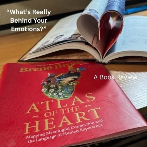 A red book titled "Atlas of the Heart" by Brené Brown on a table, with an open book in the background. The open book has a cover illustrating a heart with a ribbon and an eye inside it. Text on the image reads, "What's Really Behind Your Emotions?" and "A Book Review."
