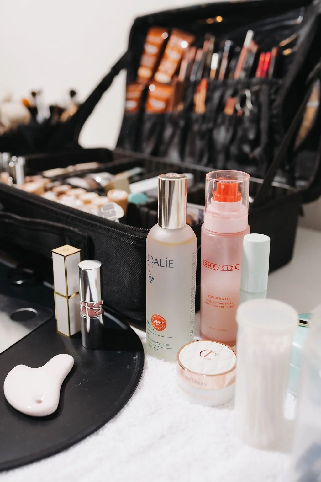 Beauty products and tools arranged on a table in front of an open makeup case filled with cosmetics and brushes.