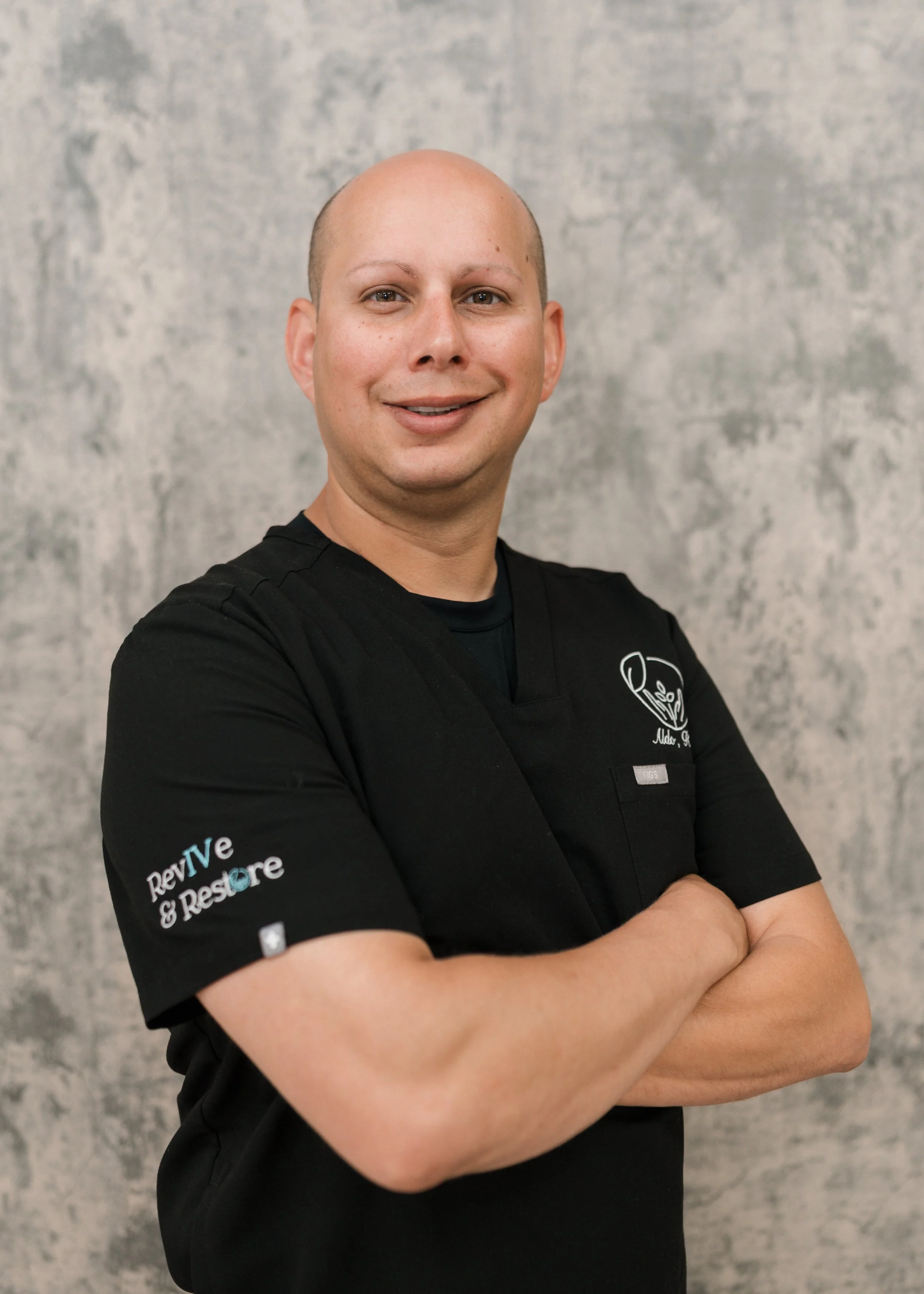 Person smiling indoors, wearing a blue jacket, with framed photos on wall in background.