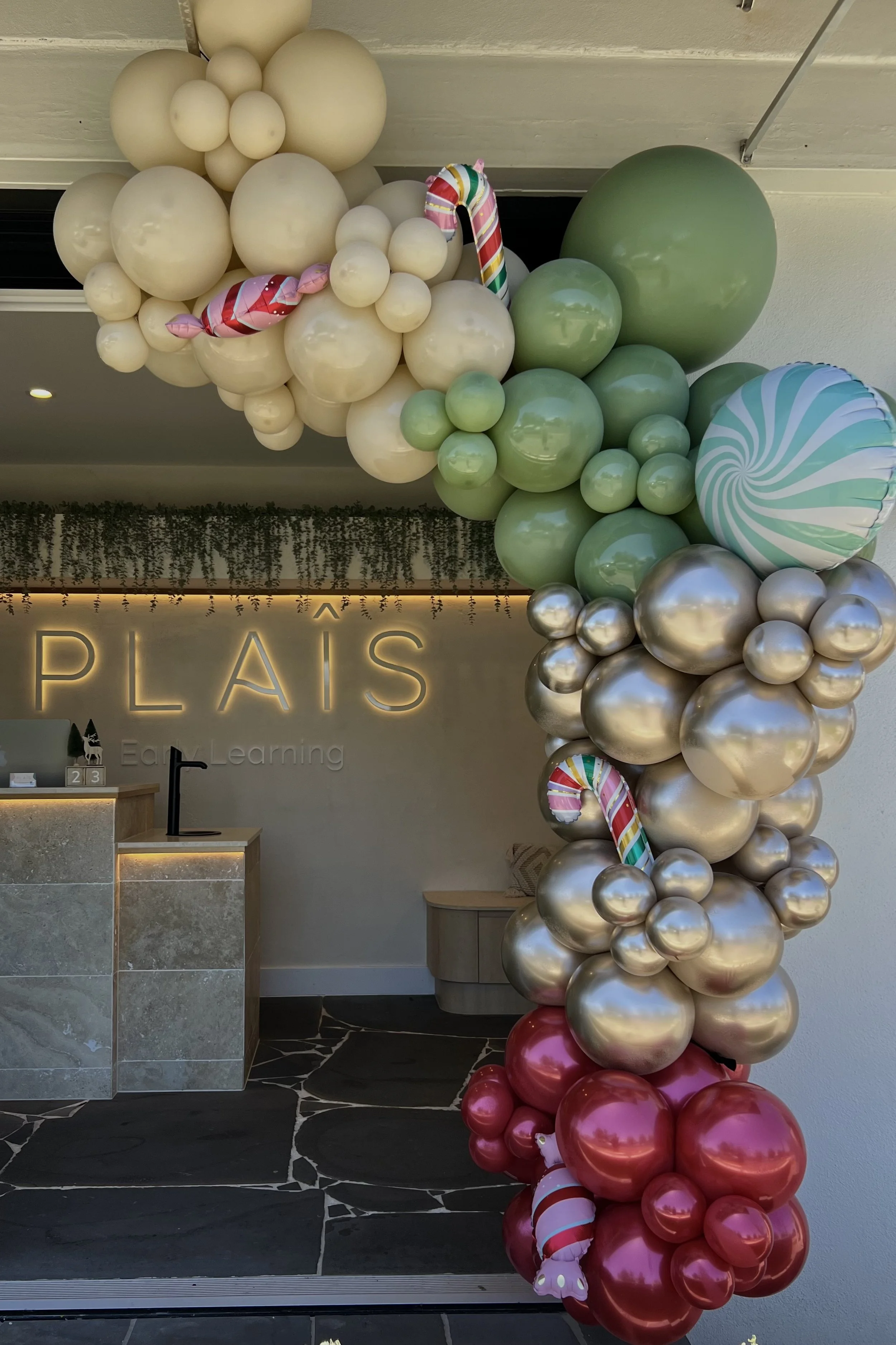 Decorative balloon arch featuring cream, silver, pink, green, and striped balloons at the entrance of Plais Early Learning center.