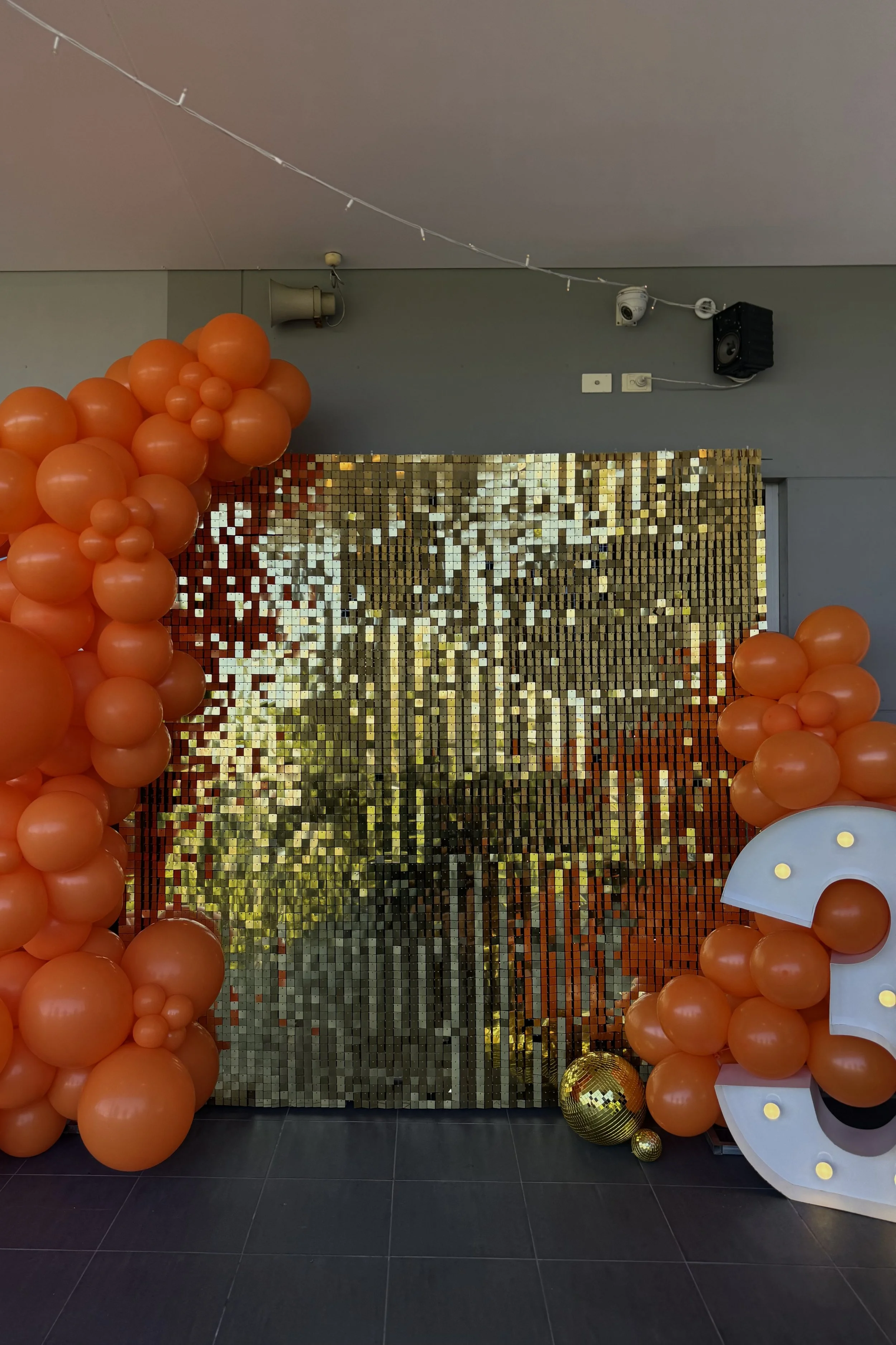 Gold shimmer wall backdropped, styled with a bright orange balloon garland and '30' light up numbers.