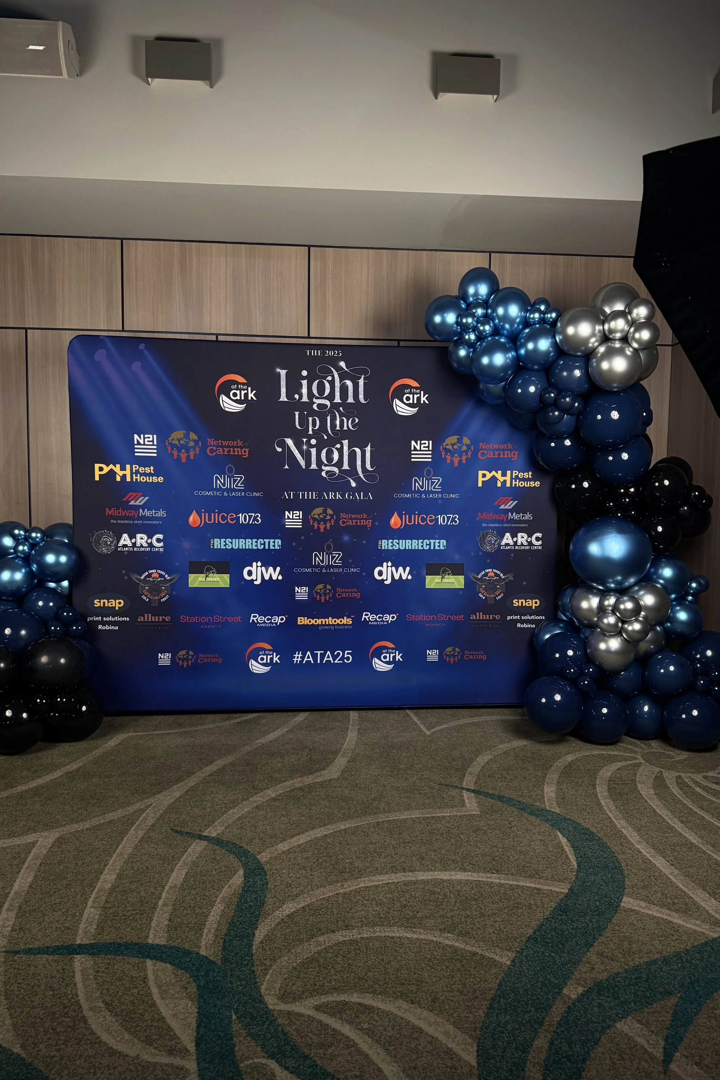 Event backdrop with sponsor logos and blue and silver balloon arrangements for 'Light Up the Night' at Ark Gala 2024.