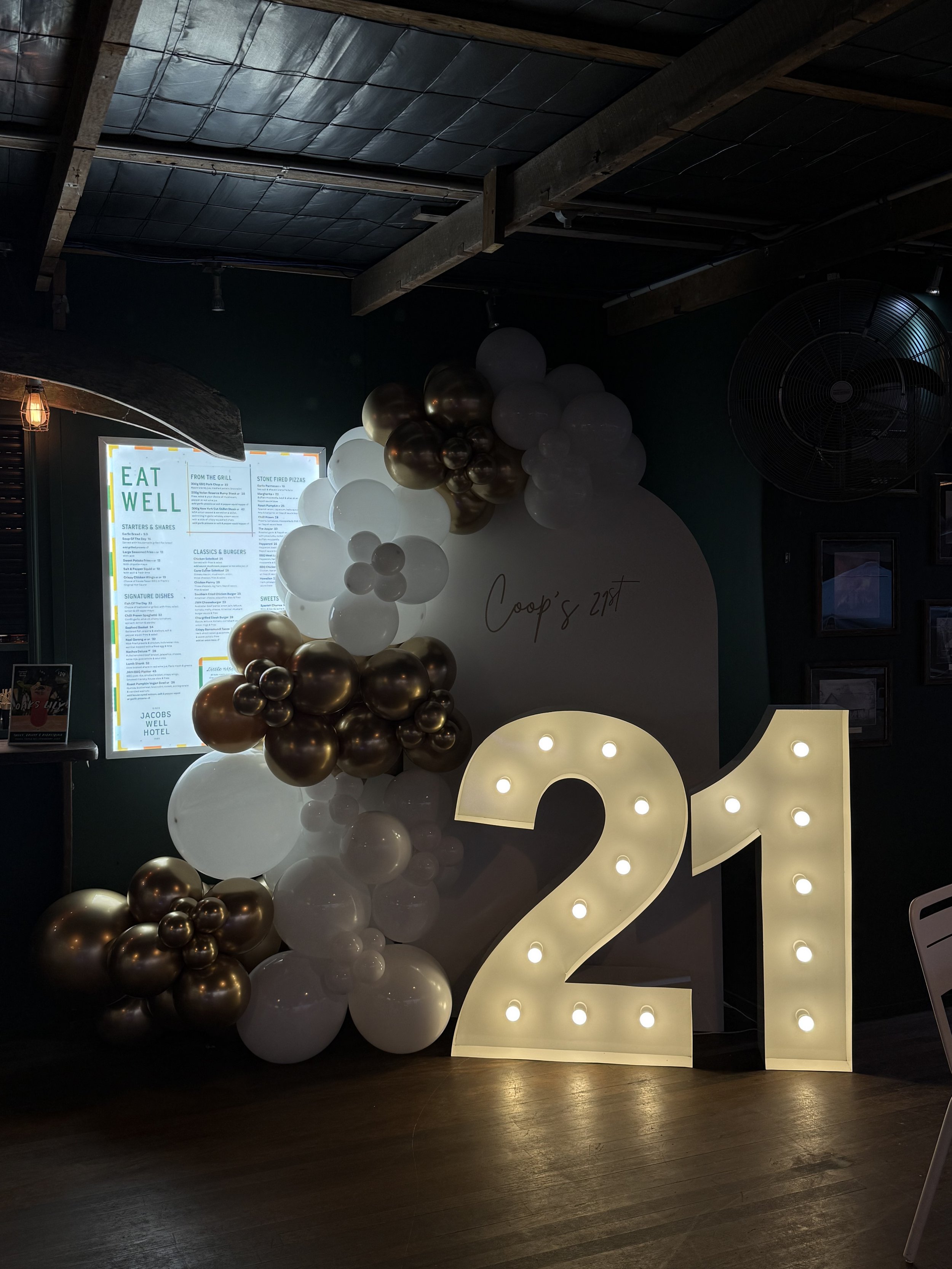 Large illuminated number 21 with a white and gold balloon garland with a custom decal.