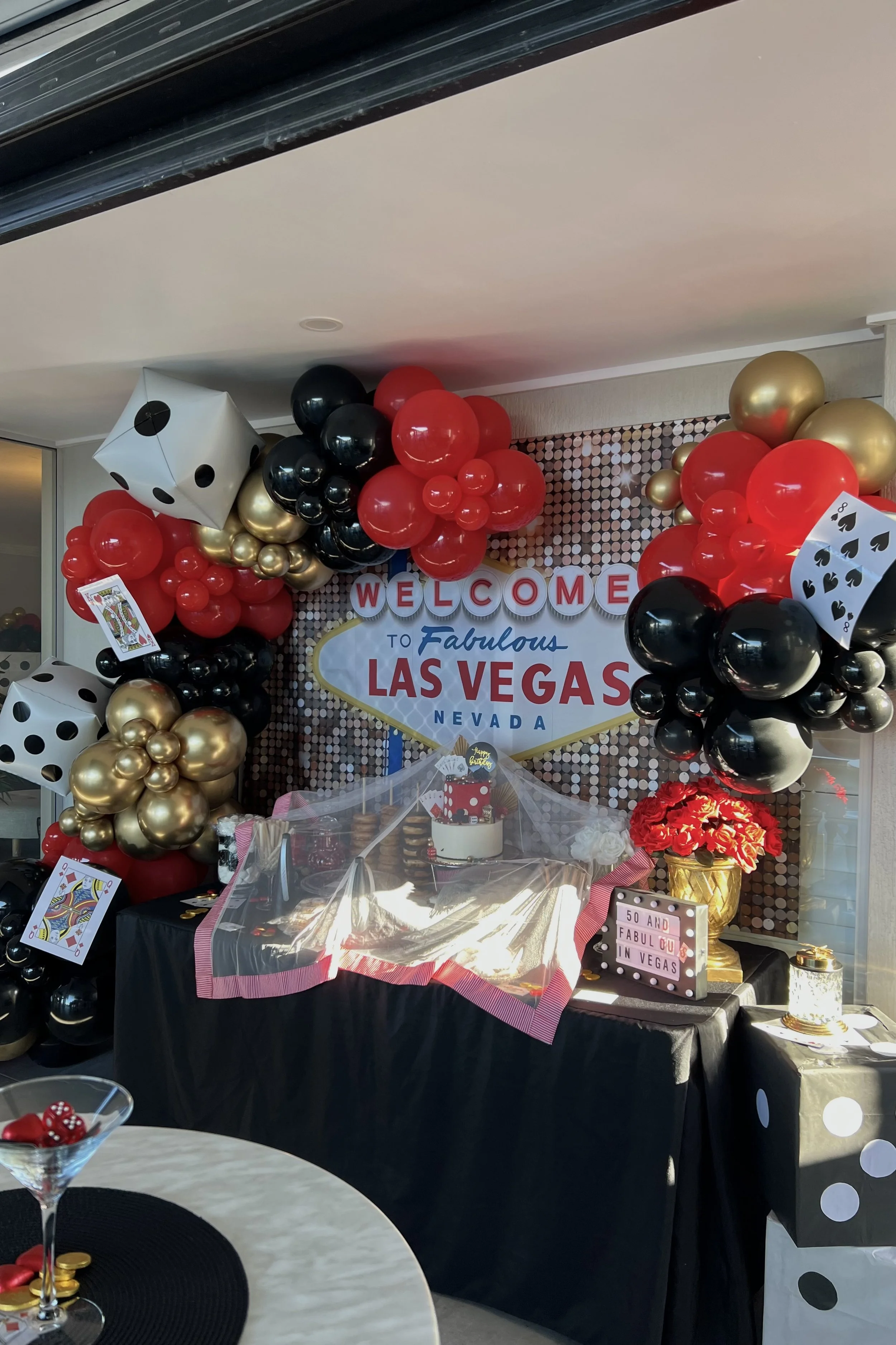 Decorative birthday celebration setup with casino-themed balloons shaped like dice, playing cards, and poker symbols, featuring a 