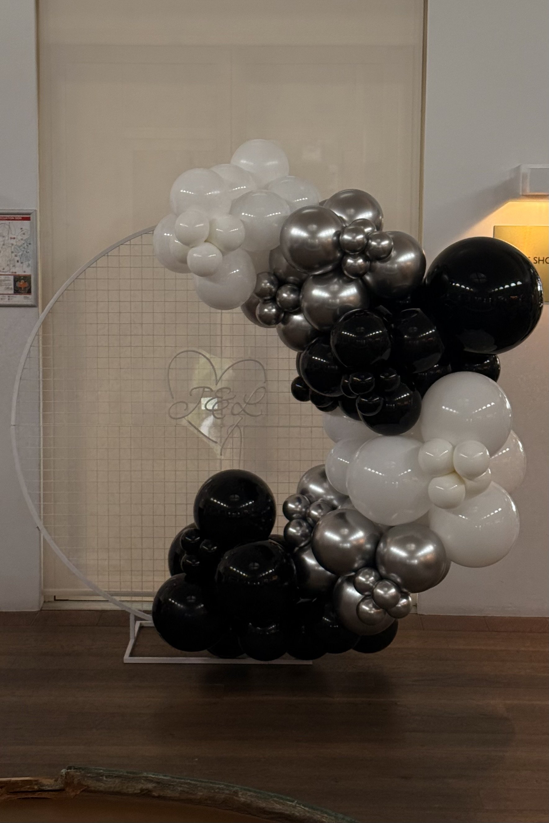 A decorative display of black, white, and metallic silver balloon garland arranged on a white circular frame.