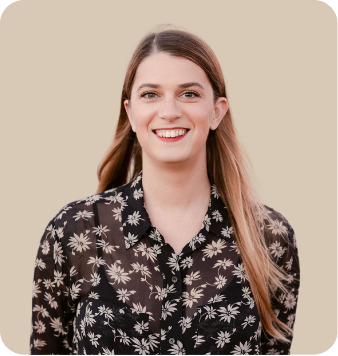 A young woman with long brown hair, smiling, wearing a black shirt with white floral pattern, against a beige background.