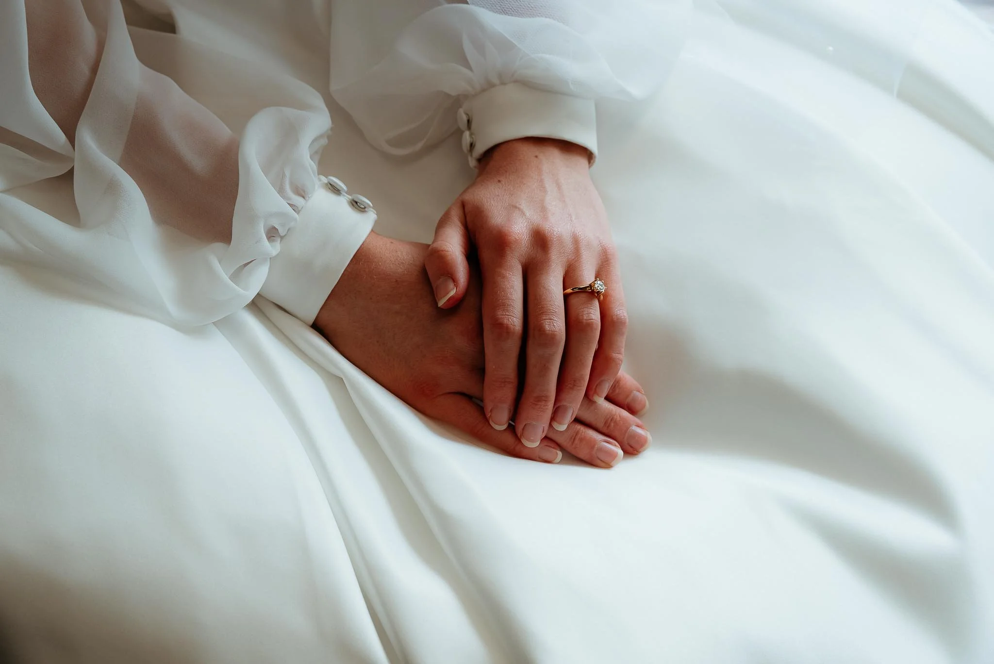 Close-up of a bride's hands resting on her wedding dress, with an engagement ring on her finger.