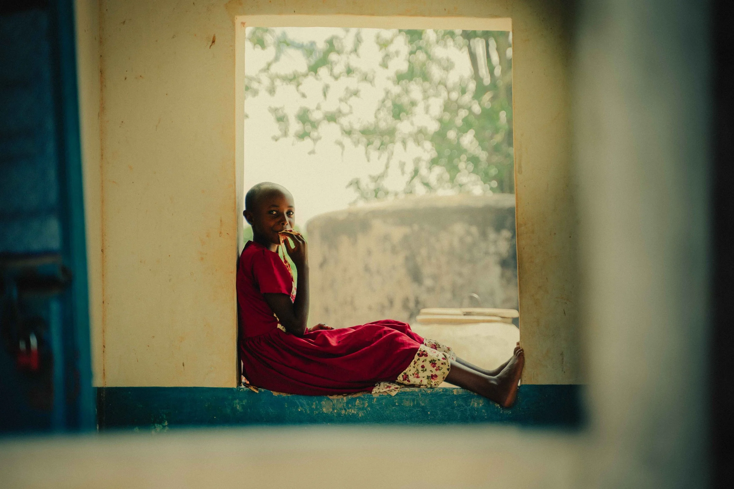 young girl in red dress sitting in window Kenya