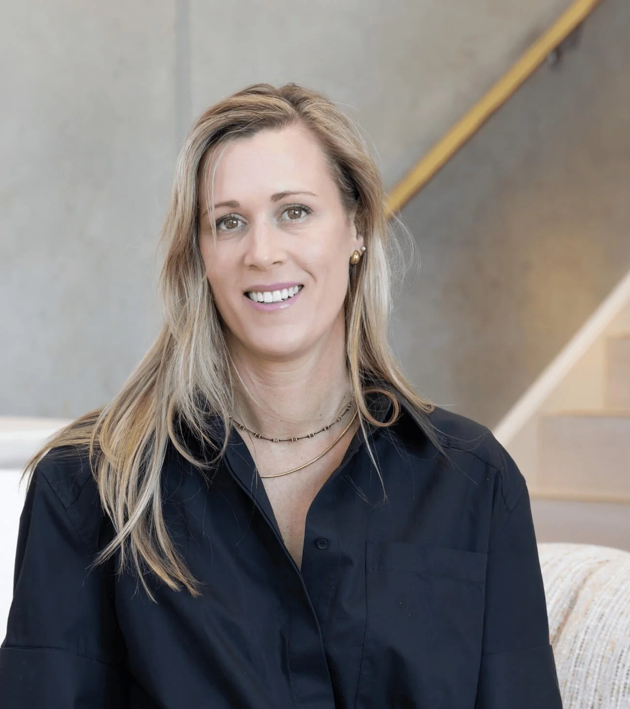 Professional portrait of Nat Eady, co-founder of Assembl Studio, seated in a modern interior space wearing a dark blouse and smiling toward camera.