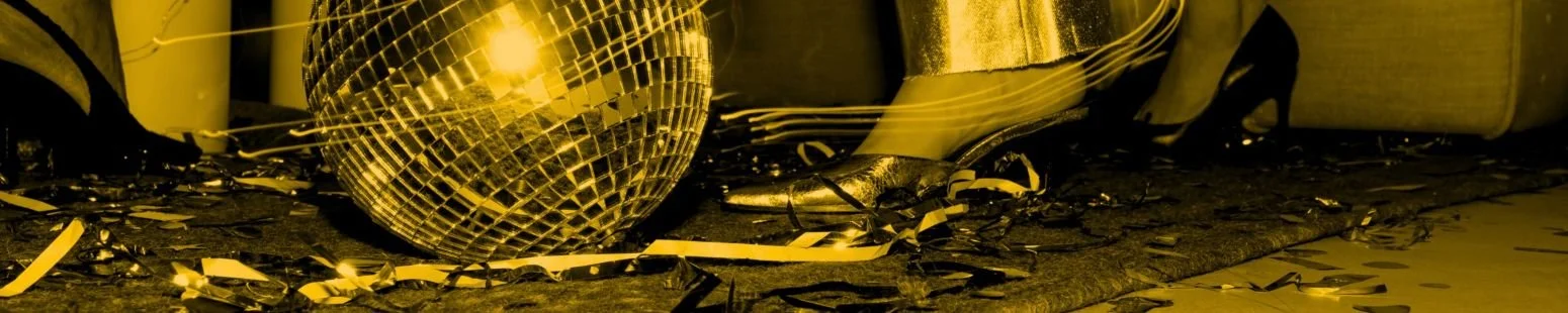 Disco ball on the floor with scattered party decorations and a person's feet in high heels at a celebration.