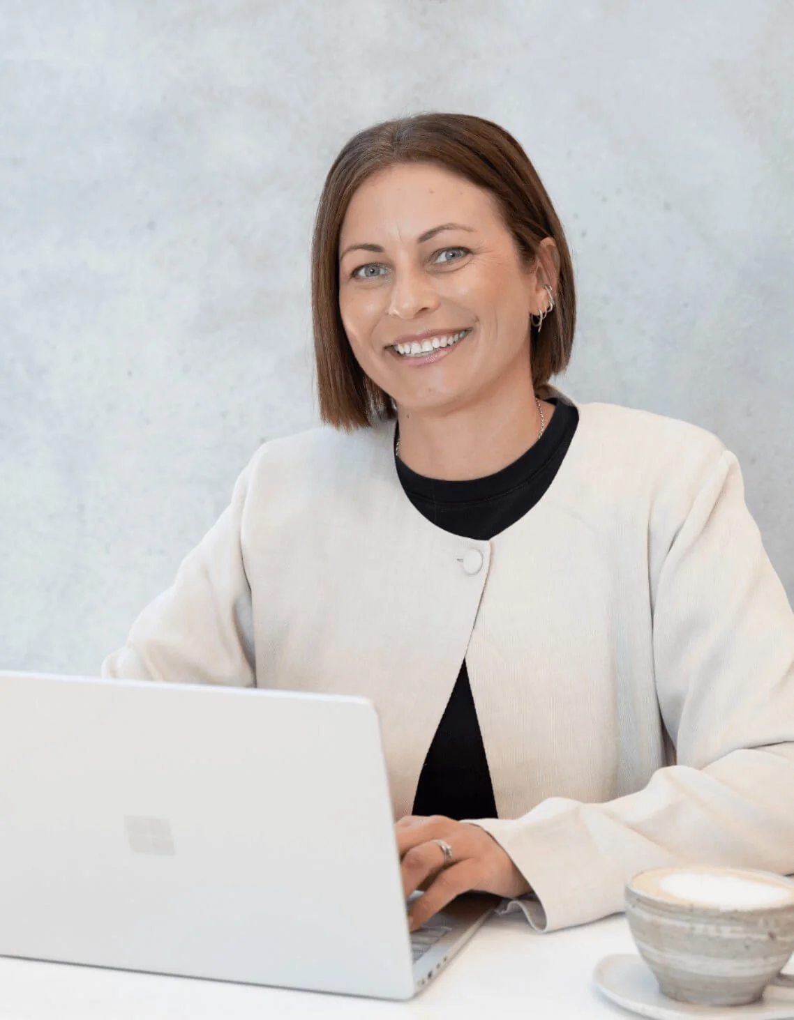 Professional portrait of Jade Burger, co-founder of Assembl Studio, smiling while seated at a desk with a laptop in a modern studio setting.