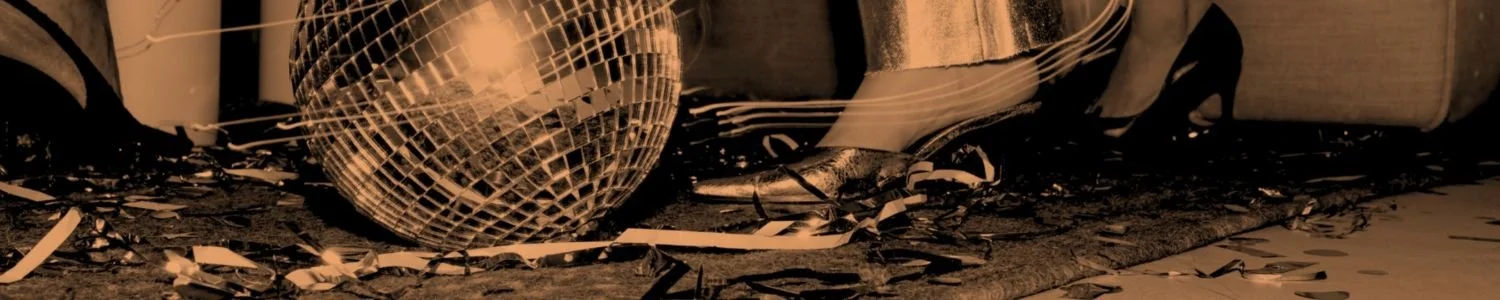 Close-up editorial image of a disco ball, metallic heels and scattered party streamers on the floor in warm monochrome lighting, used as the Assembl Studio website footer image.