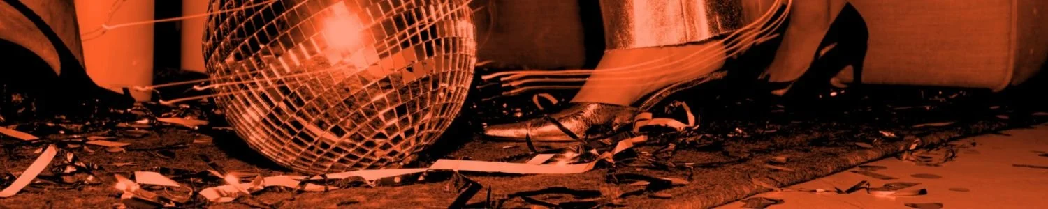 Close-up editorial image of a disco ball, metallic heels and scattered party streamers on the floor in warm monochrome lighting, used as the Assembl Studio website footer image.