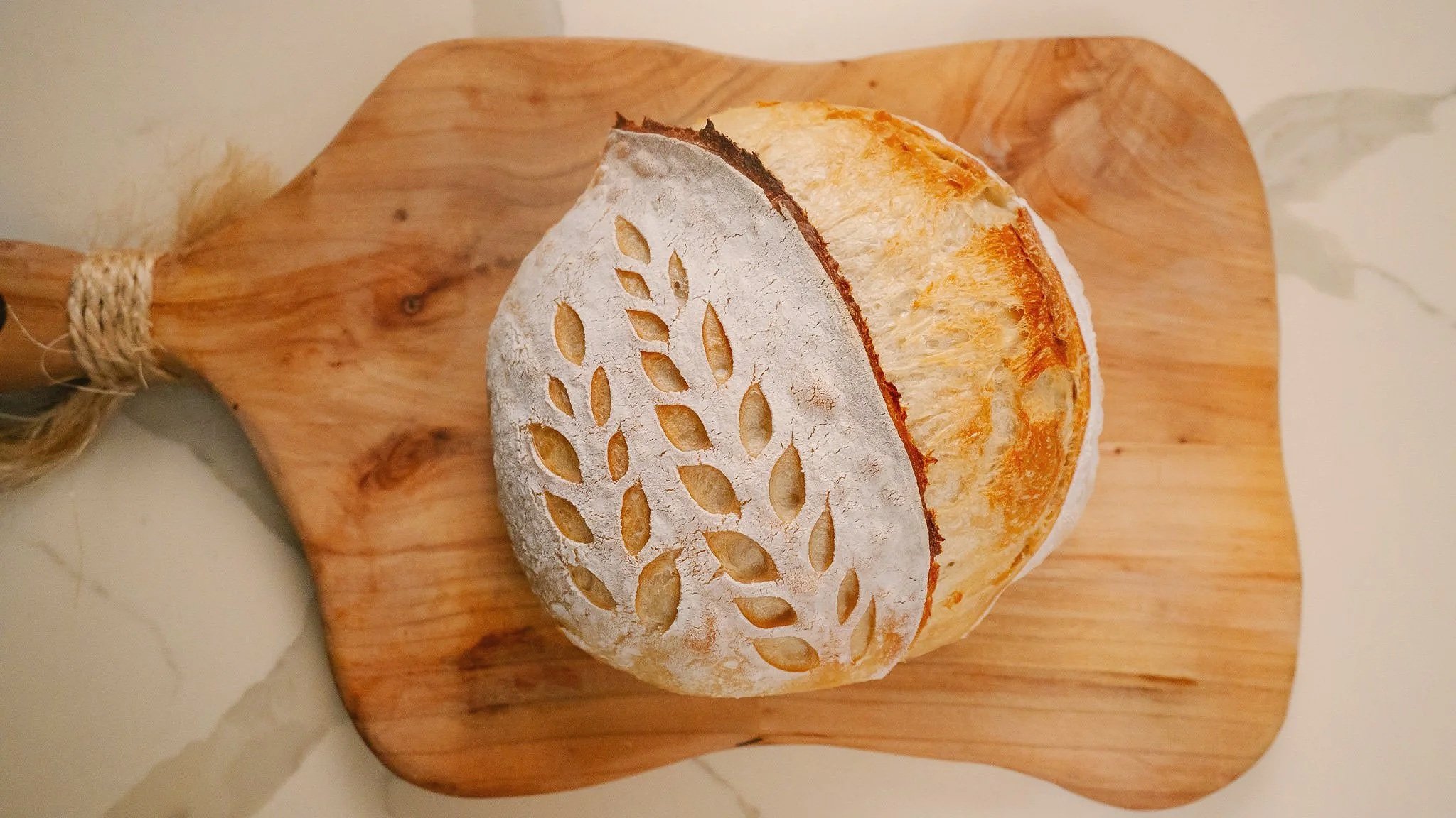 Round loaf of bread with a decorative cutout pattern on the crust, placed on a wooden cutting board.