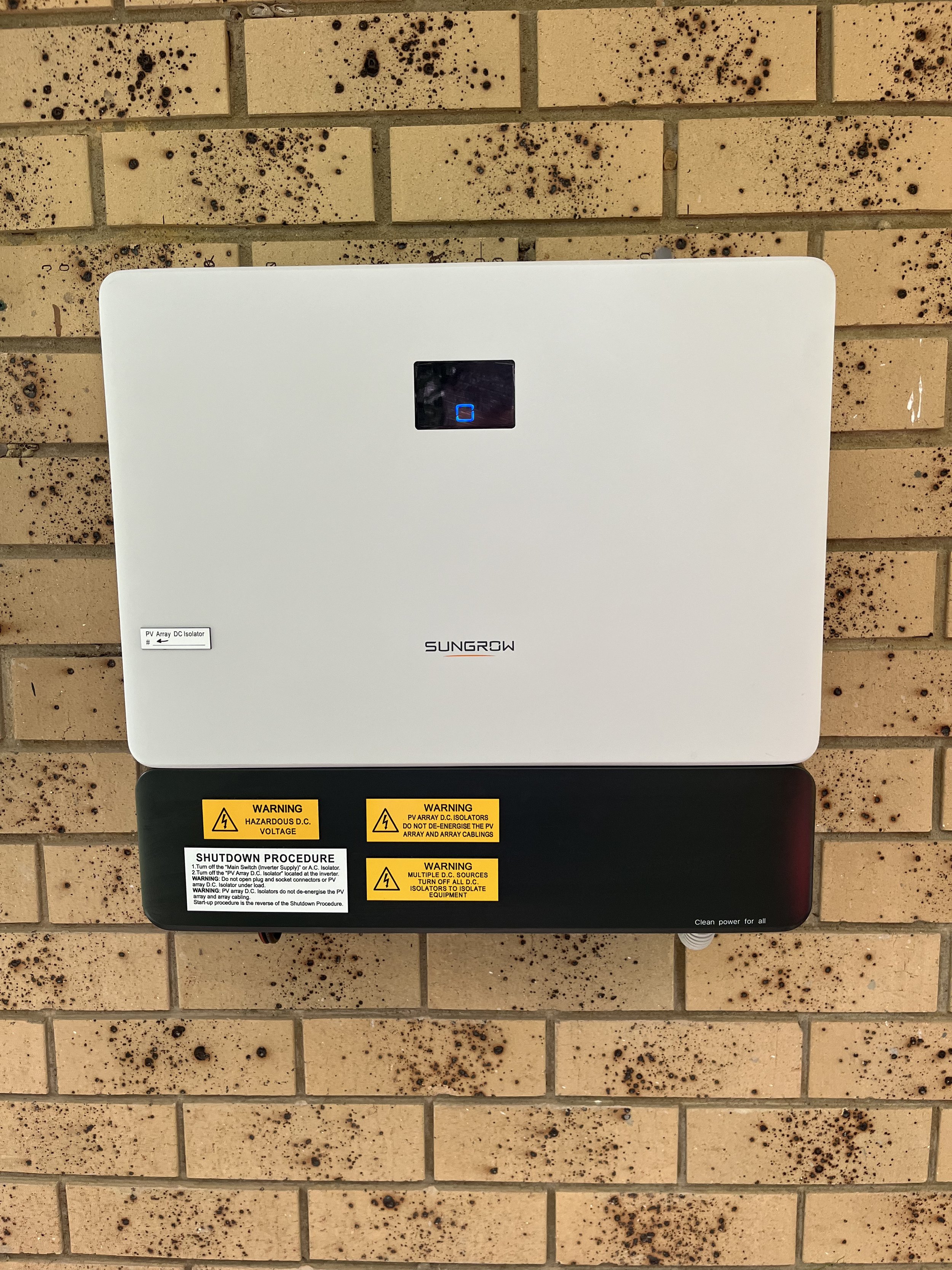 Photograph of a Sungrow solar inverter mounted on a brick wall with warning labels. Electrician Northern Rivers Electrician Northern Rivers Commercial electrician Northern Rivers Emergency electrician Northern Rivers
