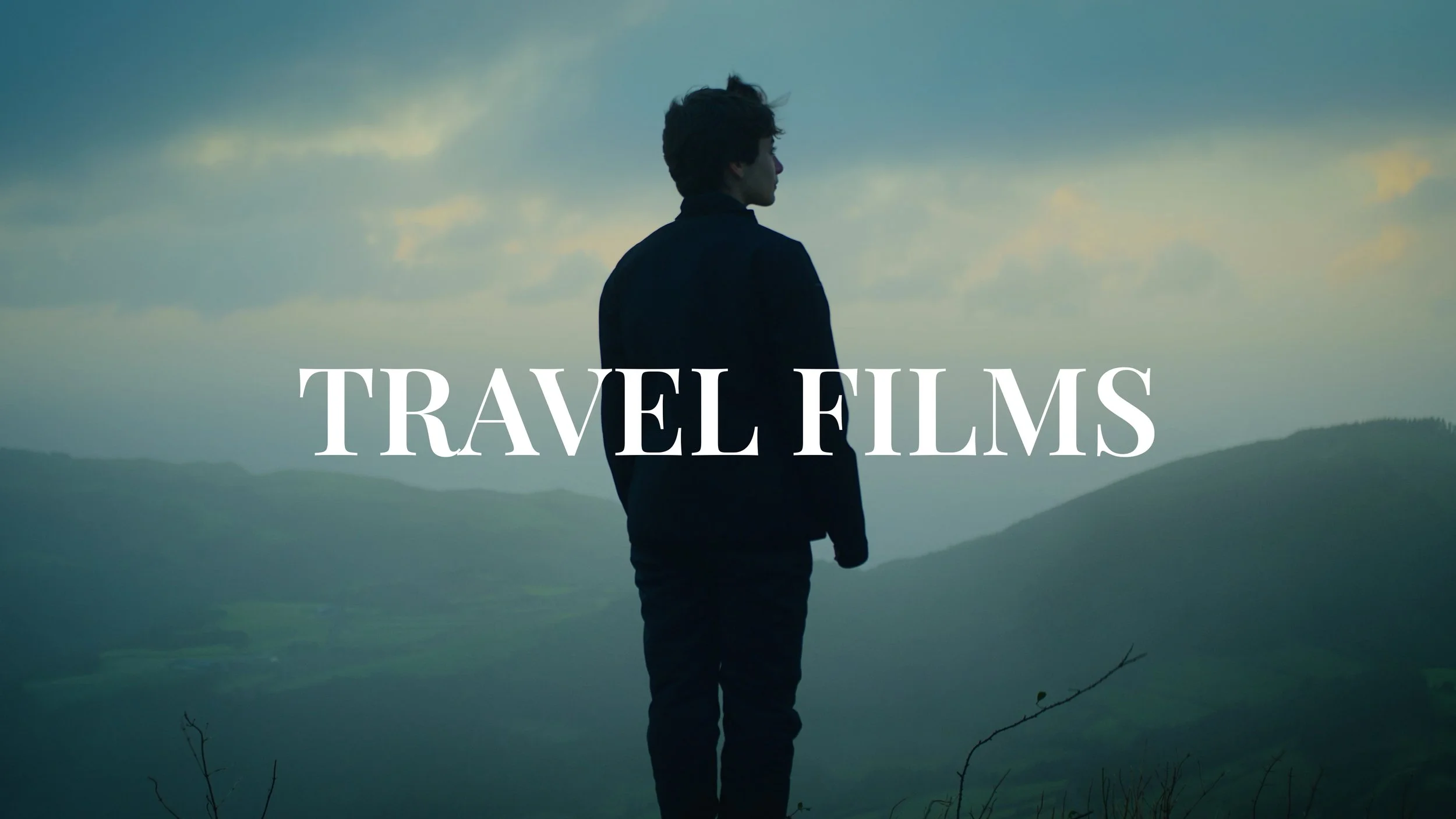 A person standing outdoors on a hilltop overlooking a landscape with hills and clouds, with white text on the image that reads 'TRAVEL FILMS'.
