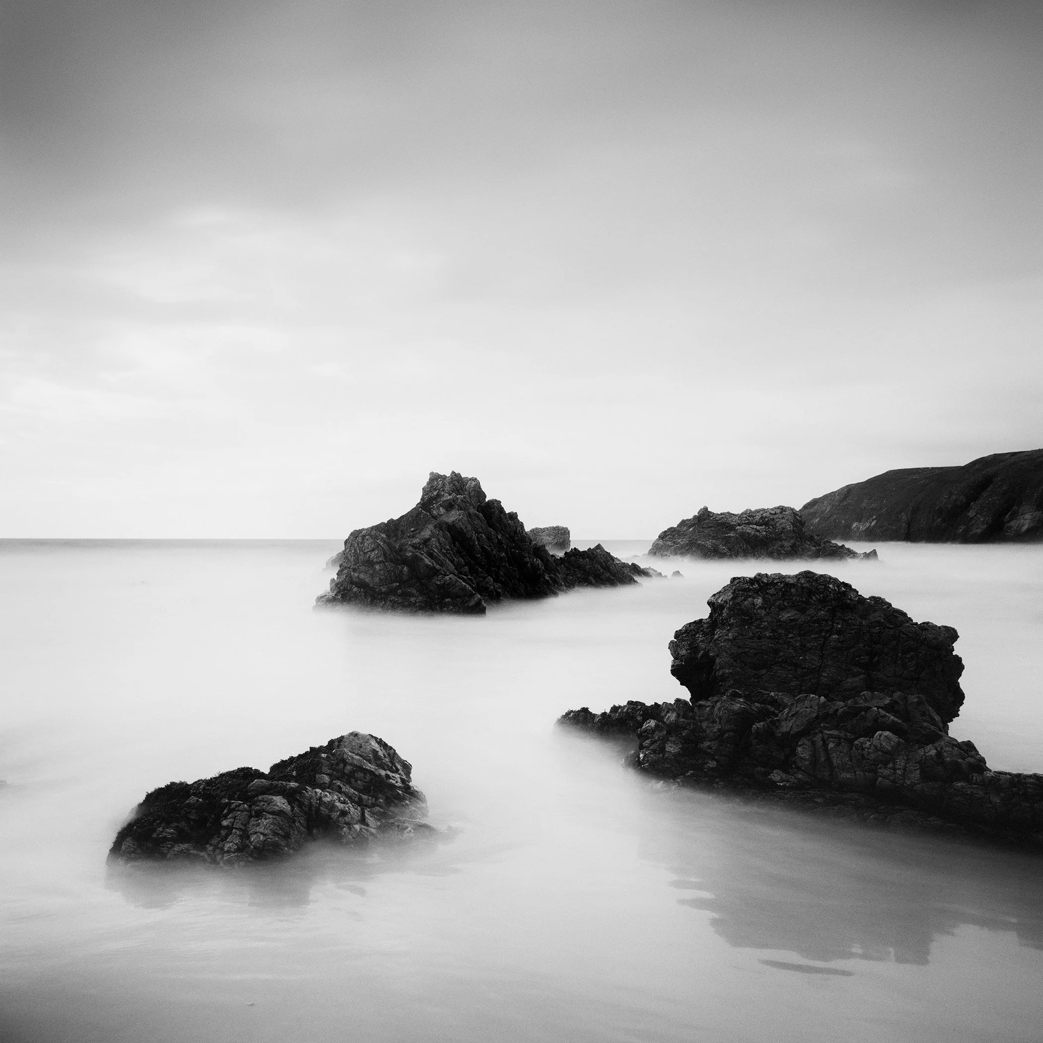Black-and-white seascape photograph of coastal rocks and smooth sea in Scotland by Gerald Berghammer