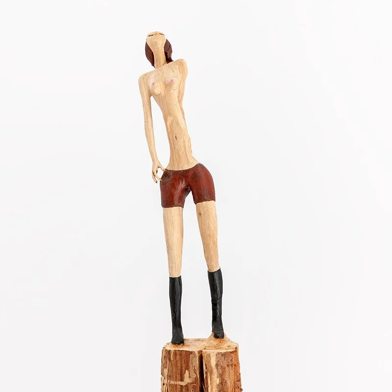 Wooden sculpture of a female figure in red shorts and black stockings by Austrian artist ToPu – Thomas Pusswald.