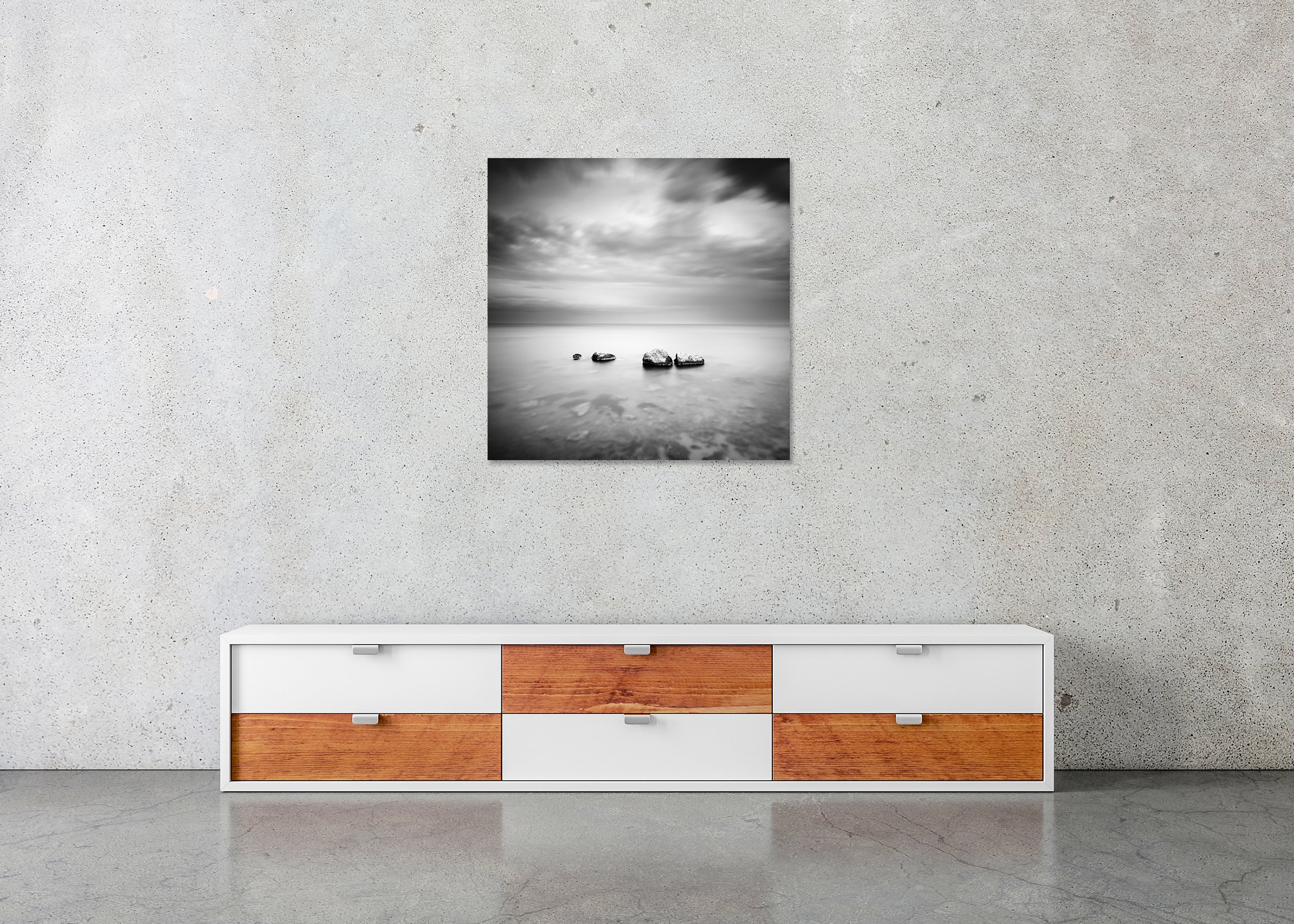 Black and white long-exposure seascape with four rocks in calm water beneath a cloudy sky, printed on frameless ChromaLuxe metal.
