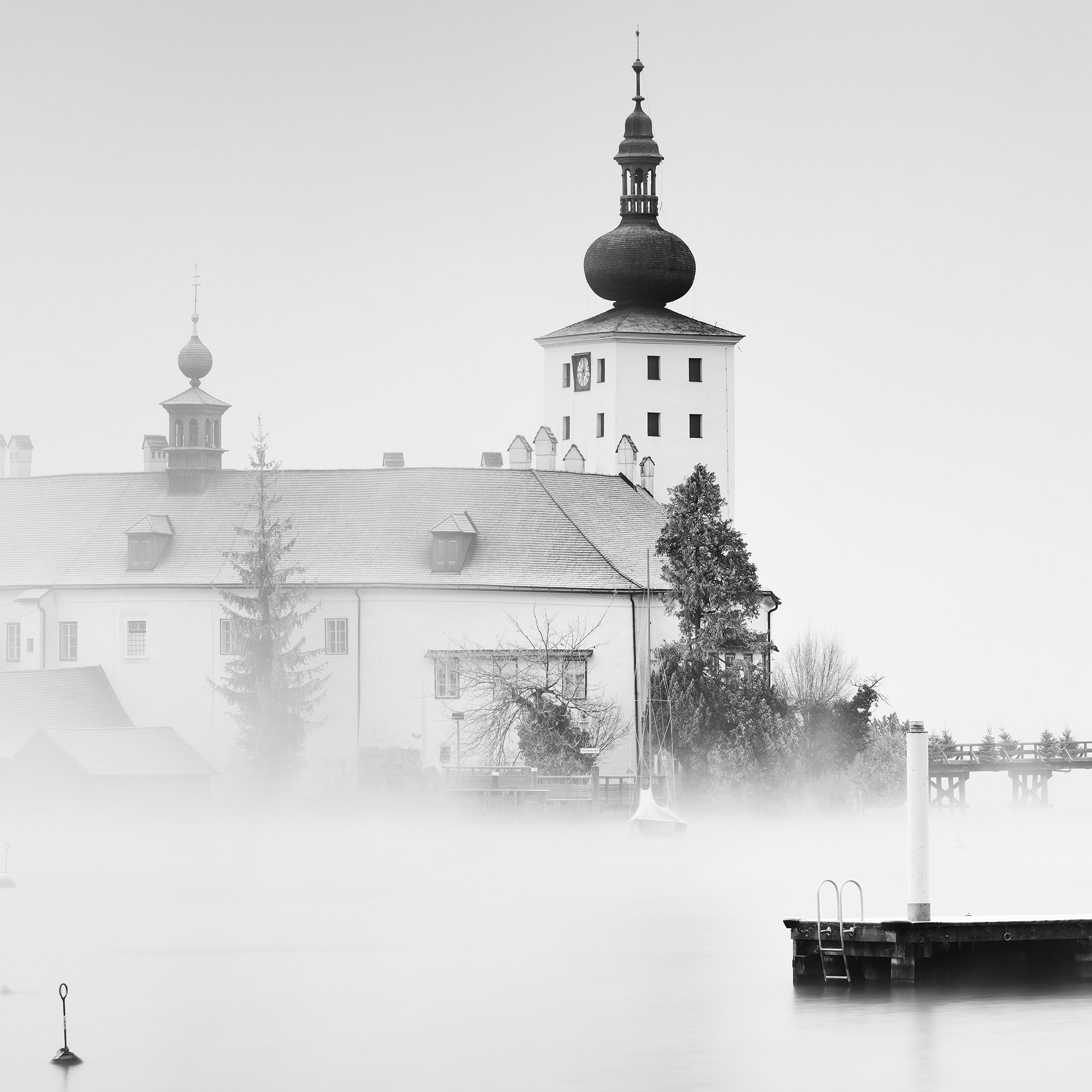 © 2022 Gerald Berghammer - Black and white cityscape photography. Schloss Ort - The historic church surrounded by mist over a lake with docks in the foreground. Print detail 3