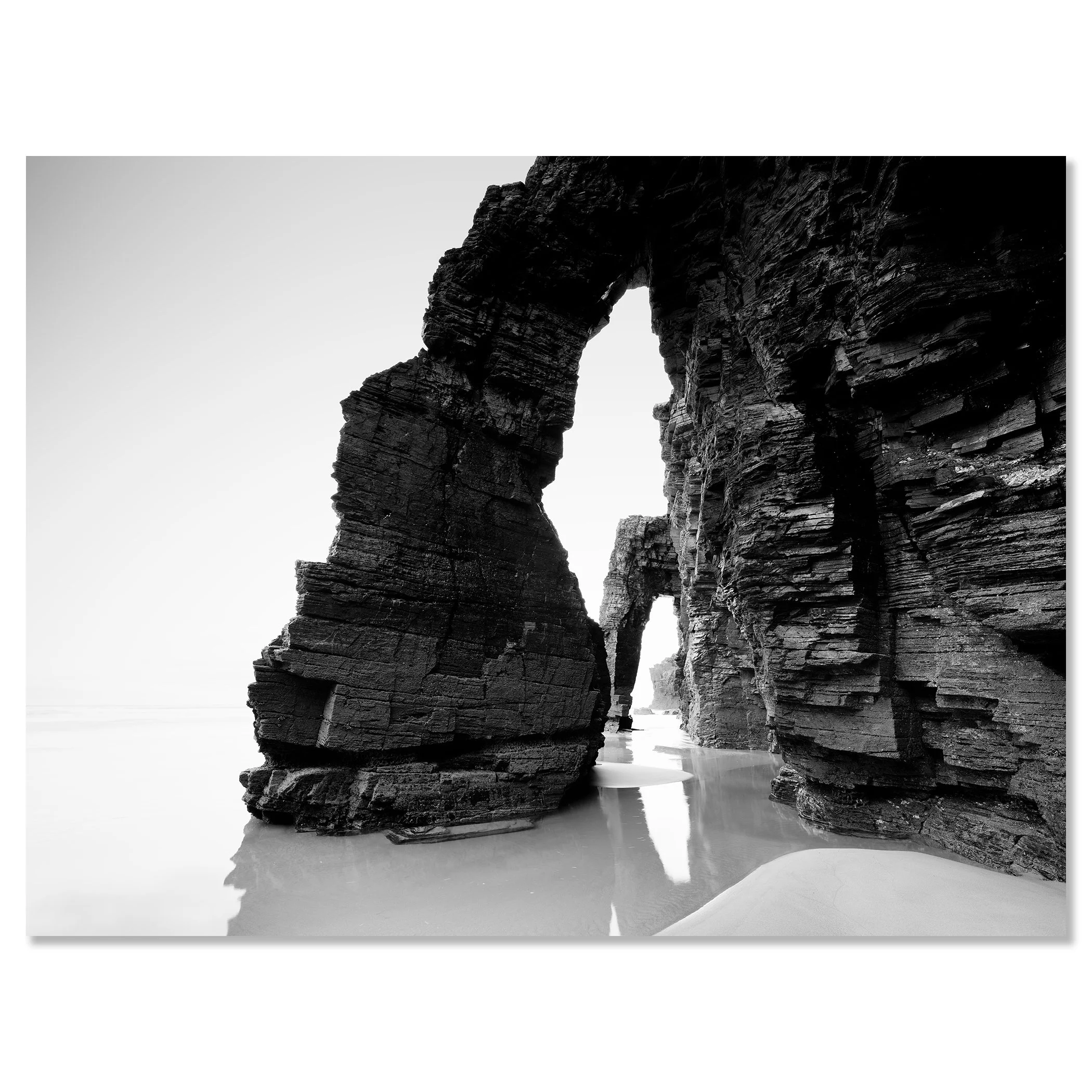 Gerald Berghammer - Black and white beach seascape photography. Large natural rock arch formations on a beach with water reflecting the rocks. Chromaluxe frameless
