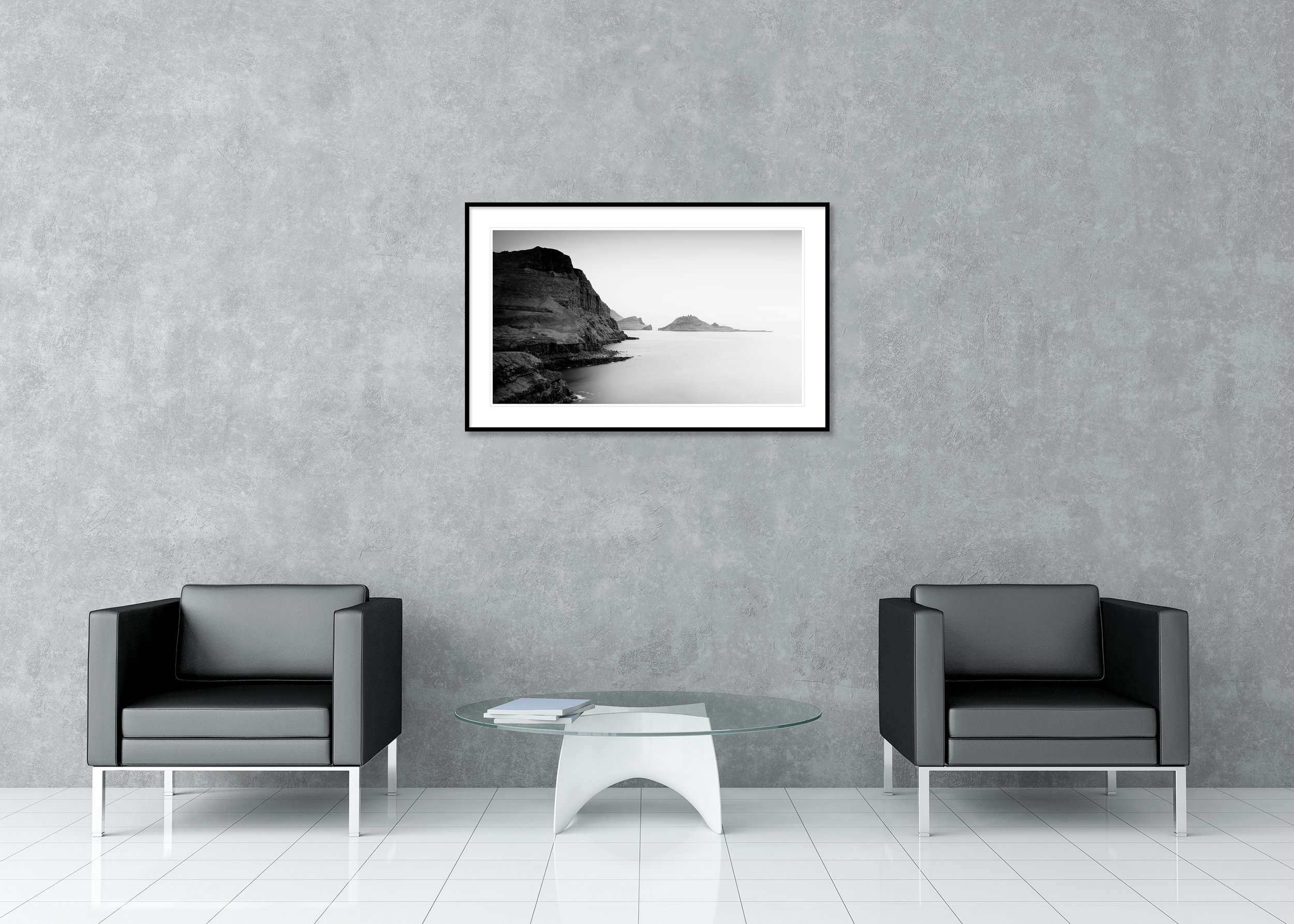 Rugged seaside cliffs and layered rock islands in a calm ocean, black and white archival pigment print in a classic frame with a mount.